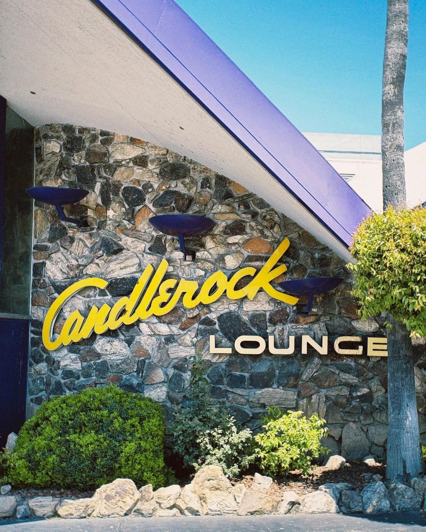 Yellow cursive Candlerock Lounge sign on a stone wall with a purple roofline.