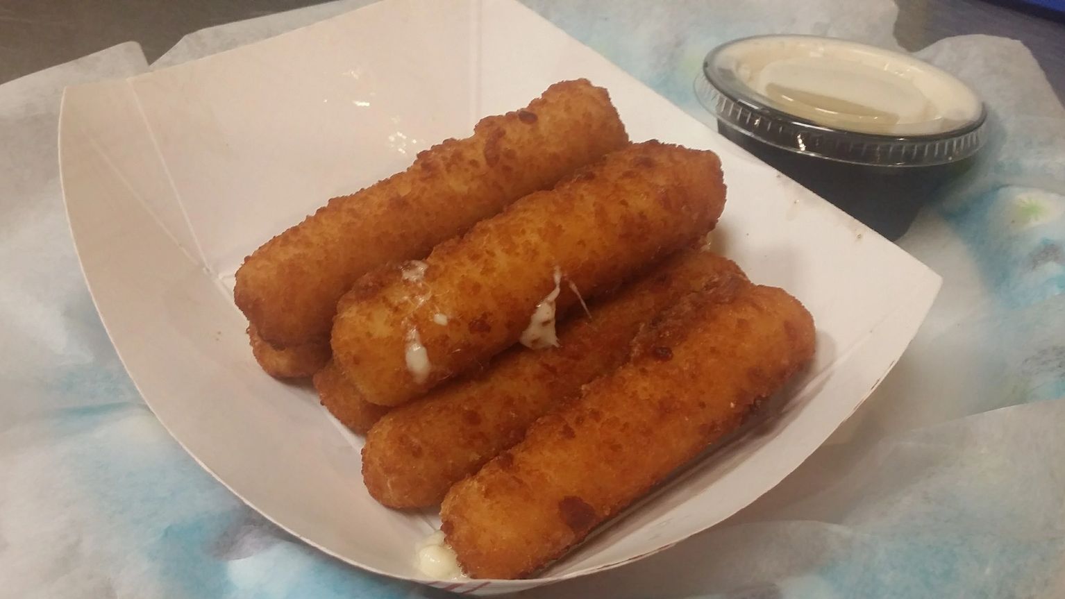 Close-up of golden mozzarella sticks in a white paper serving tray with dipping sauce.