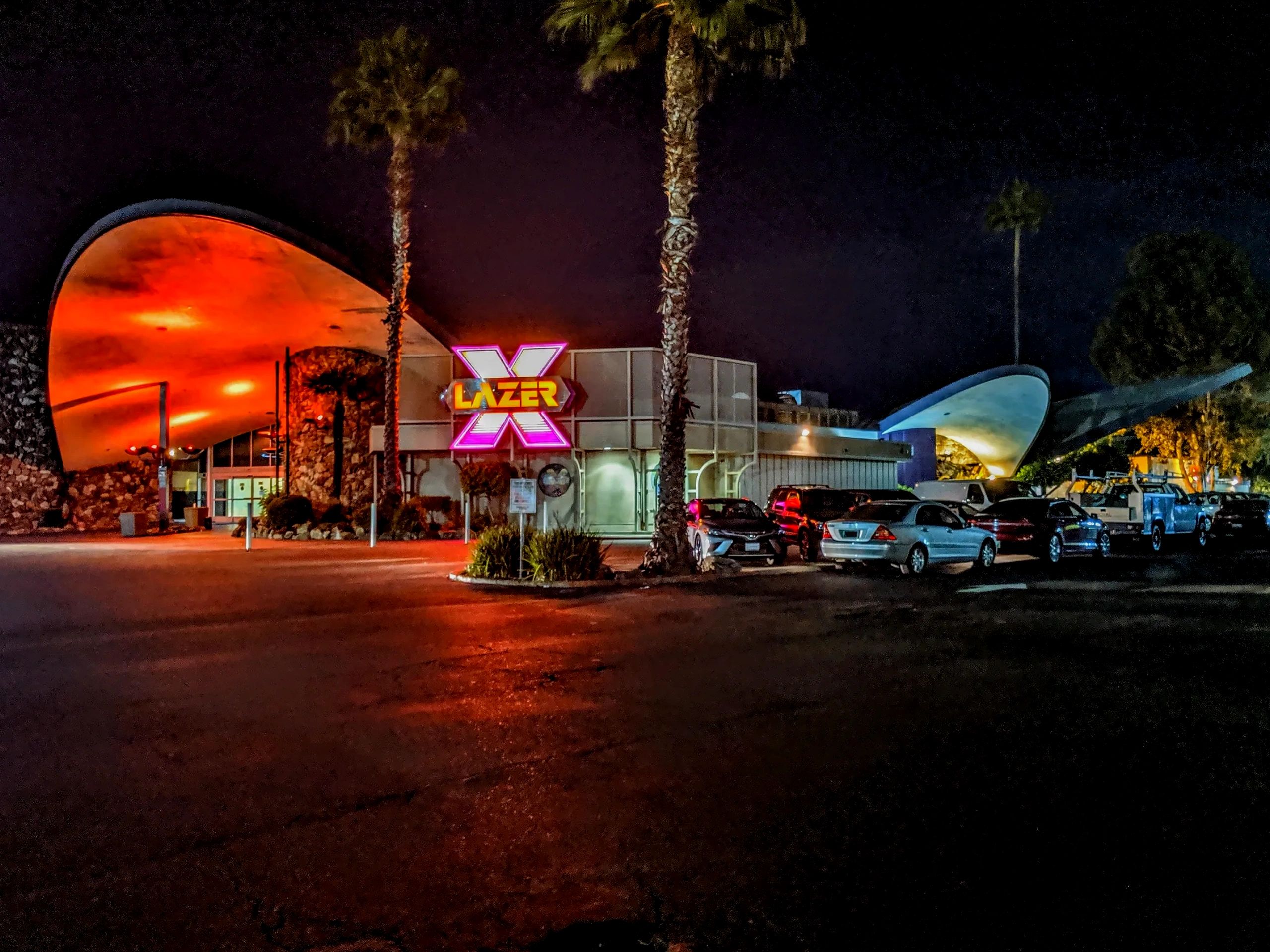 The neon Lazer X sign and orange-lit Googie-style architecture of Country Club Lanes at night.
