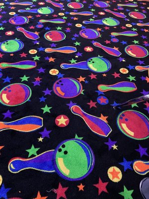 Close-up of a black carpet featuring neon bowling pins, bowling balls, and stars.