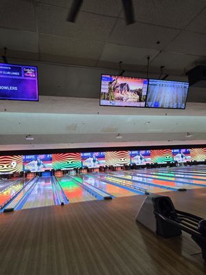 Bowling lanes with colorful light reflections and large video screens at the end of the lanes.