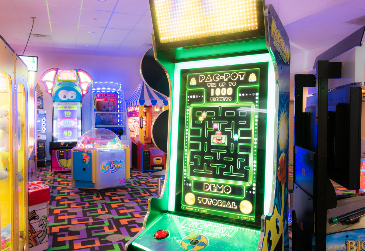 A brightly lit arcade room with various glowing ticket redemption games and a colorful geometric patterned carpet.