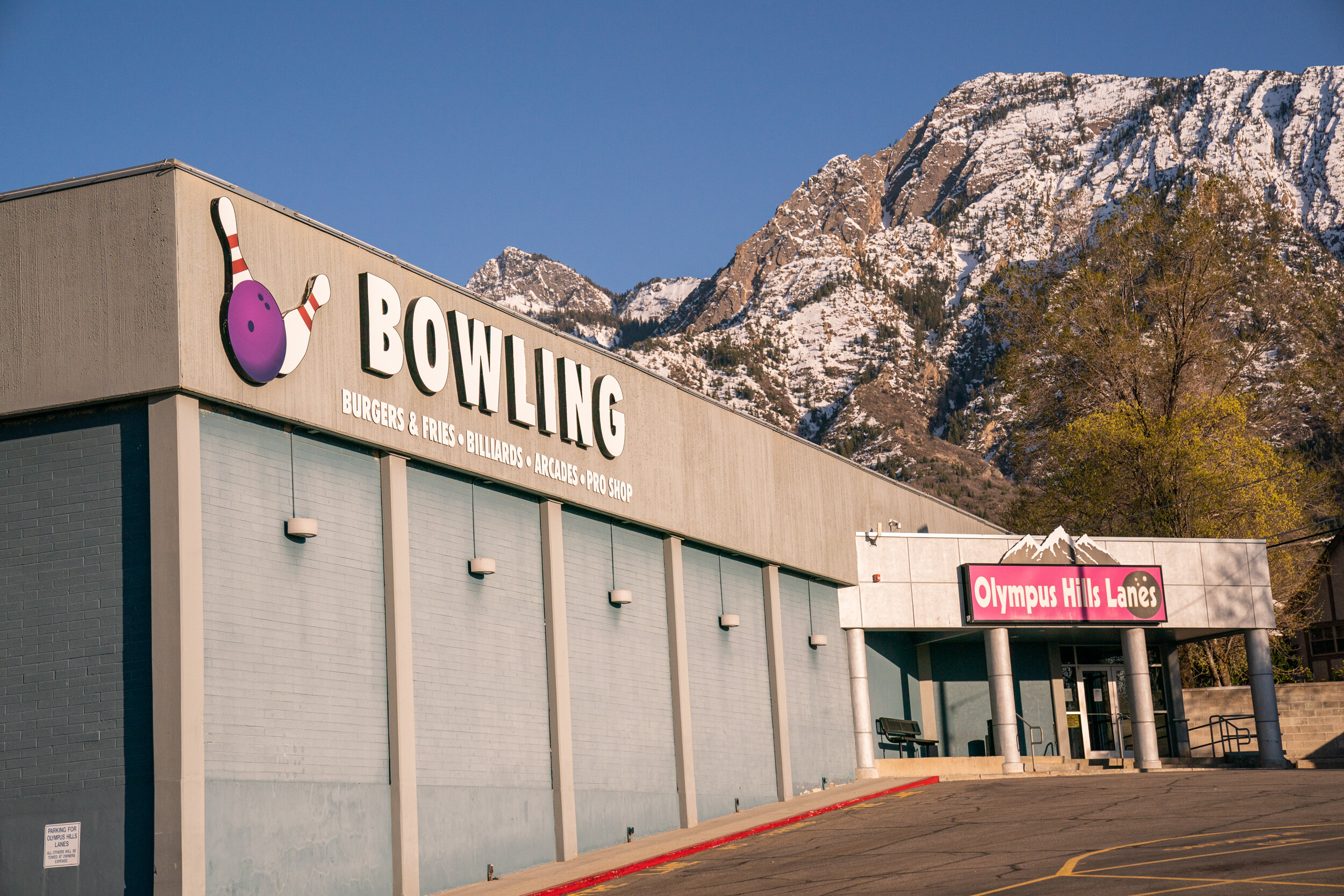 The exterior of Olympus Hills Bowling Lanes with a large white sign and snow-covered mountains in the background.