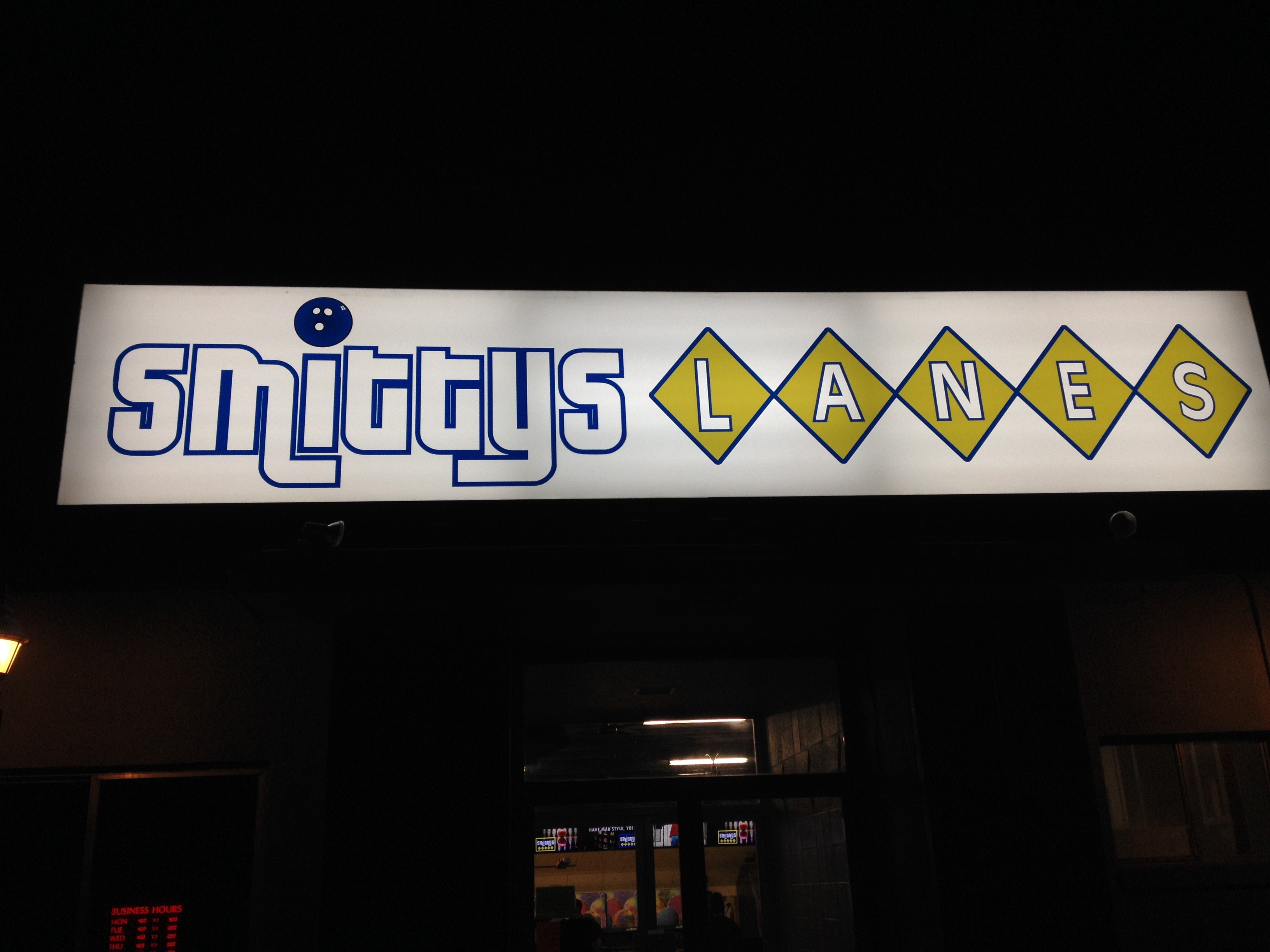 A glowing rectangular sign for Smittys Lanes with blue text and yellow diamonds against a dark night sky.