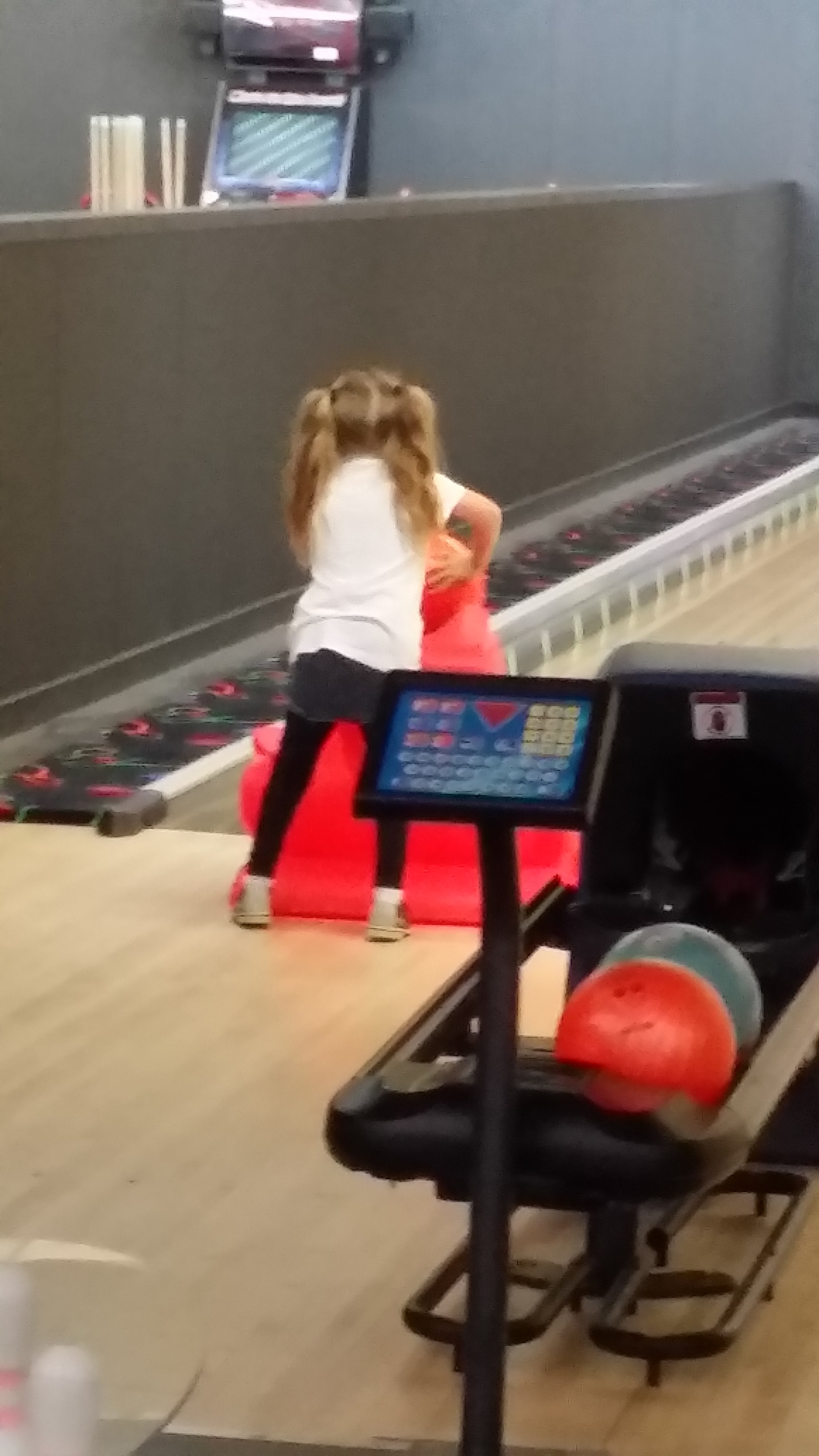 A young girl using a red dragon-shaped bowling ramp on a lane with bumpers.