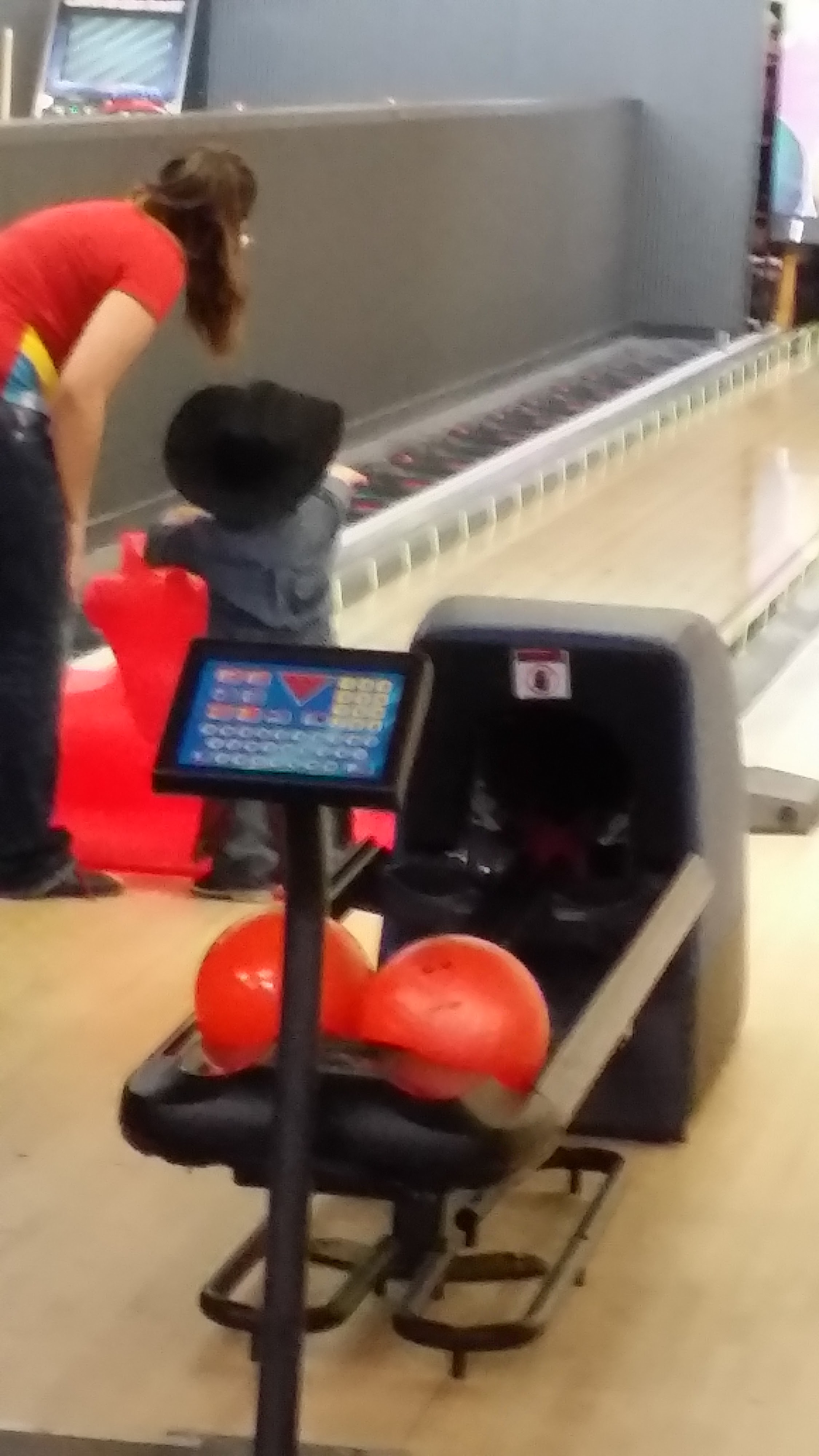 A woman and a young child use a red dragon ramp to bowl on a lane with bumper rails.