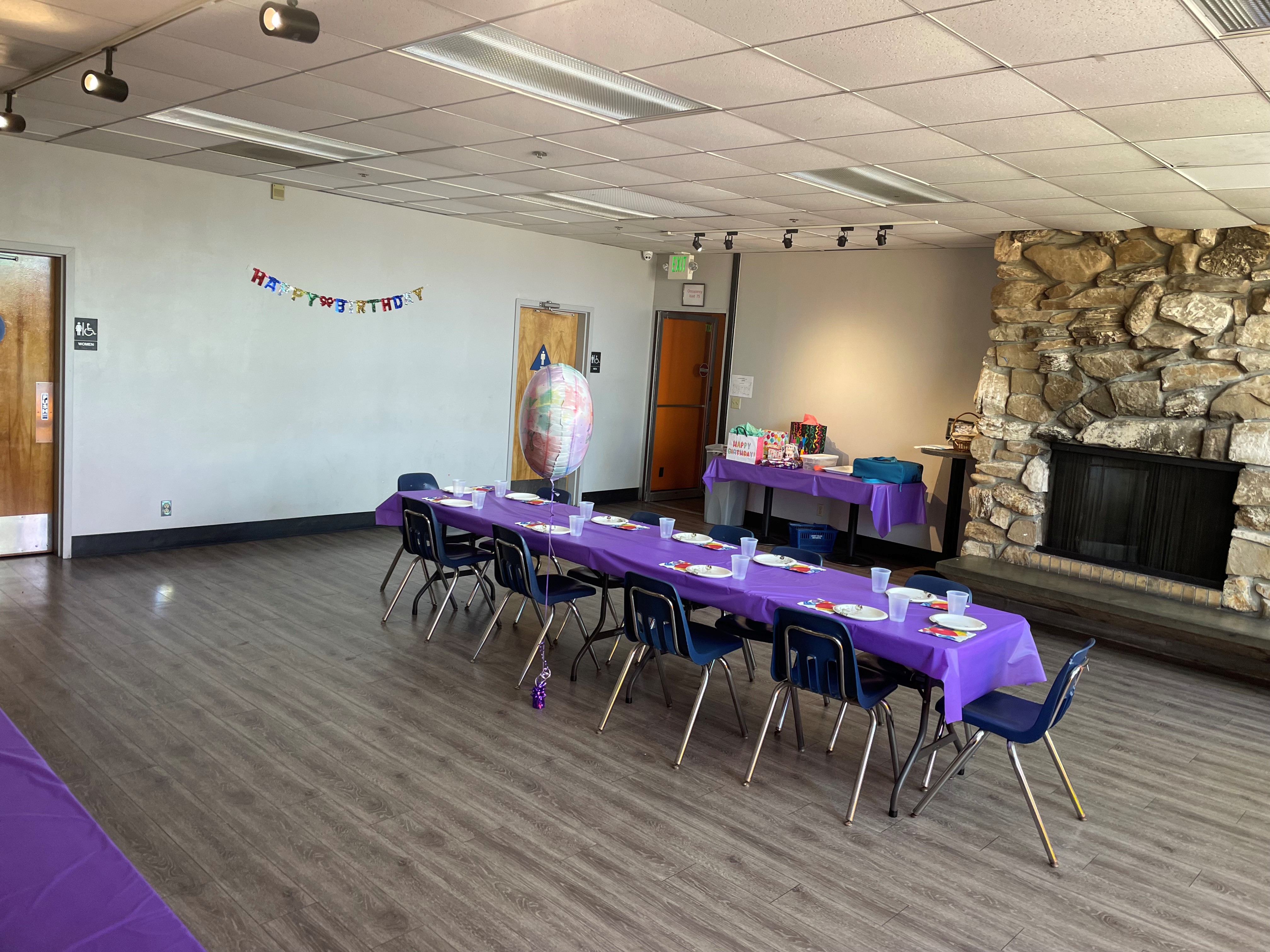 A private party room with a long table with purple tablecloths, blue chairs, and a large stone fireplace.