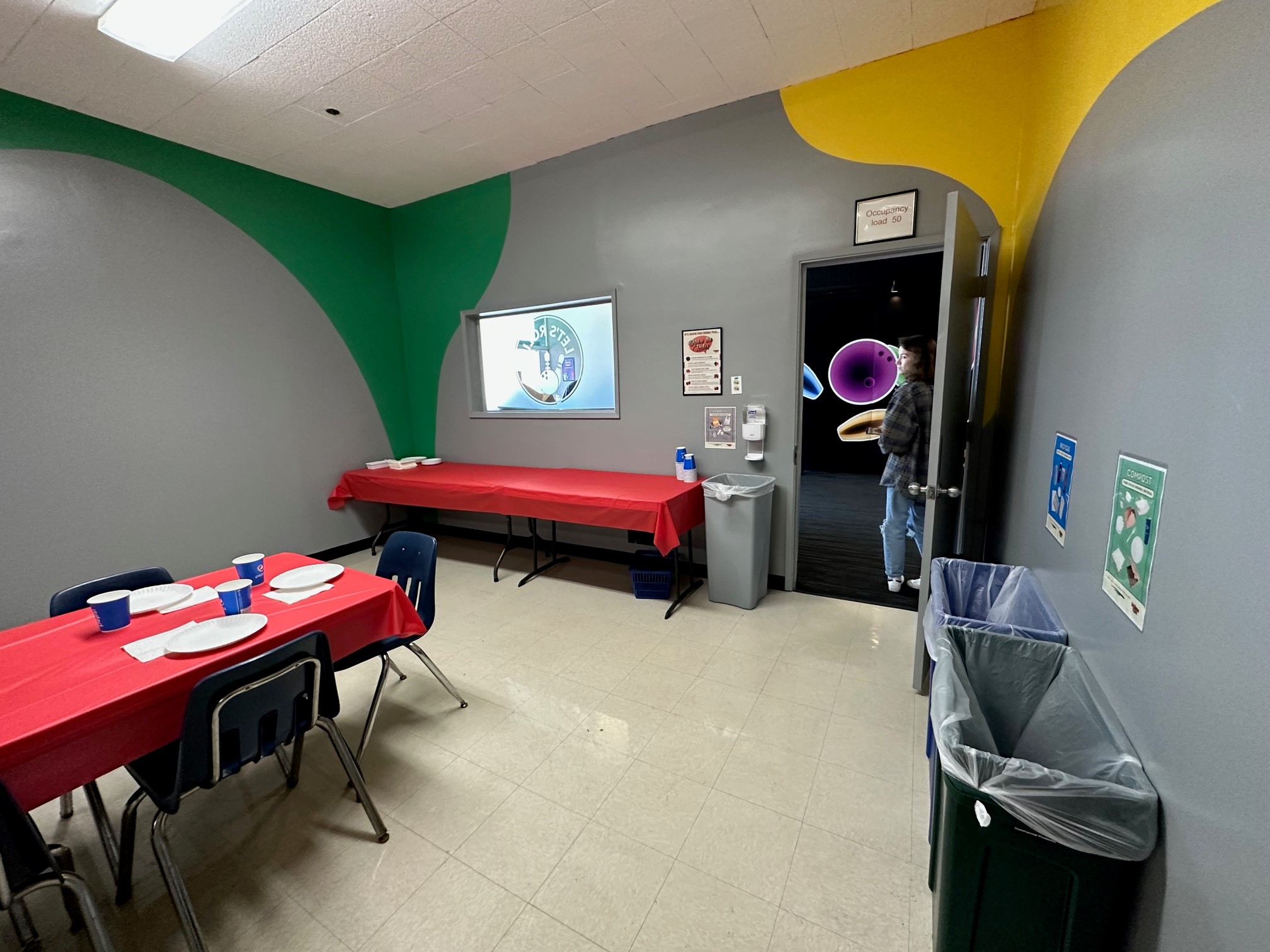 A clean bowling center party room with red-clothed tables, blue chairs, and colorful wall accents.