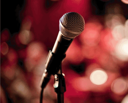 A close-up of a microphone on a stand with a blurred red and white light background.