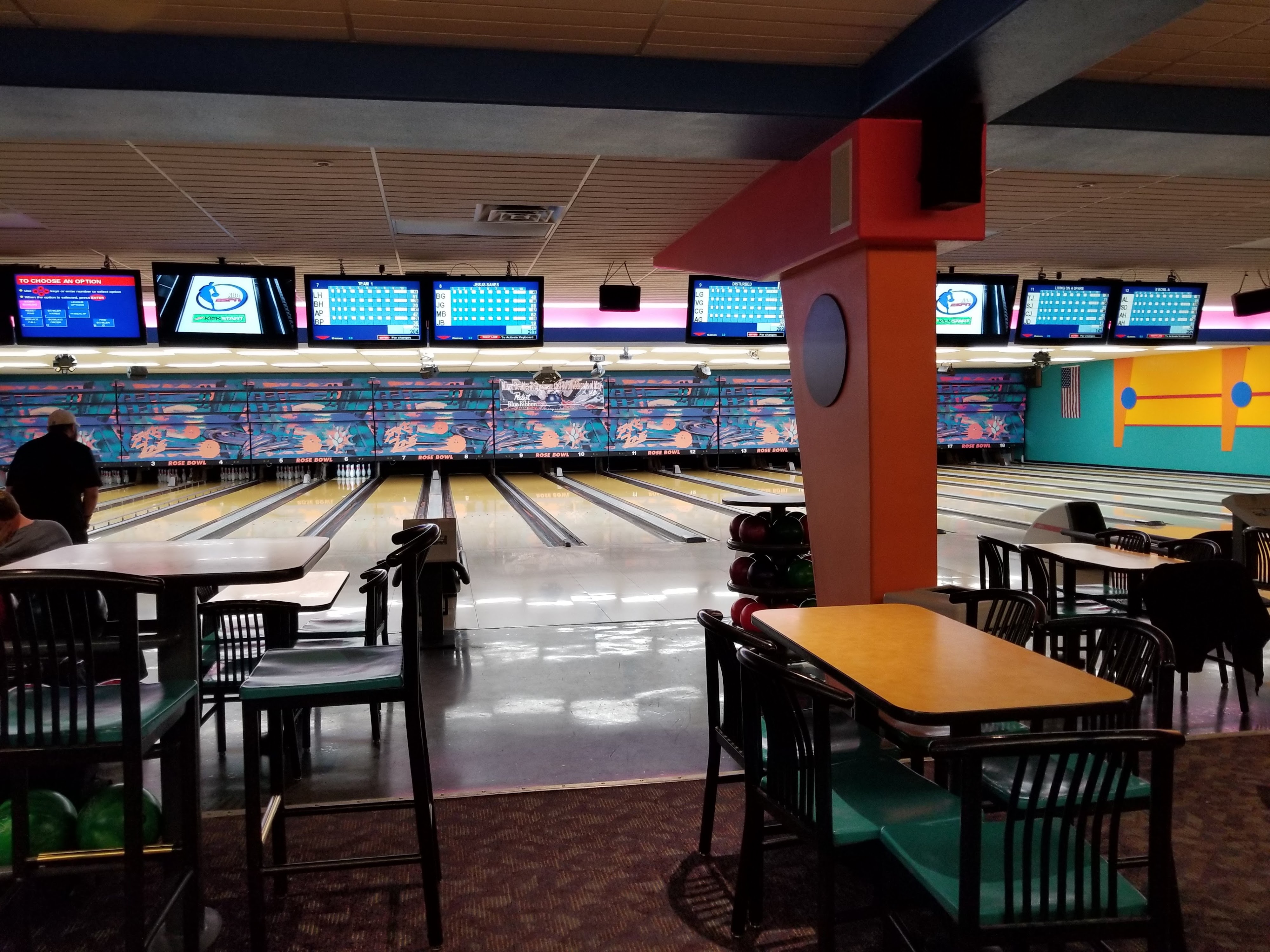 An indoor view of bowling lanes and a seating area with high-top tables at Rose Bowl.