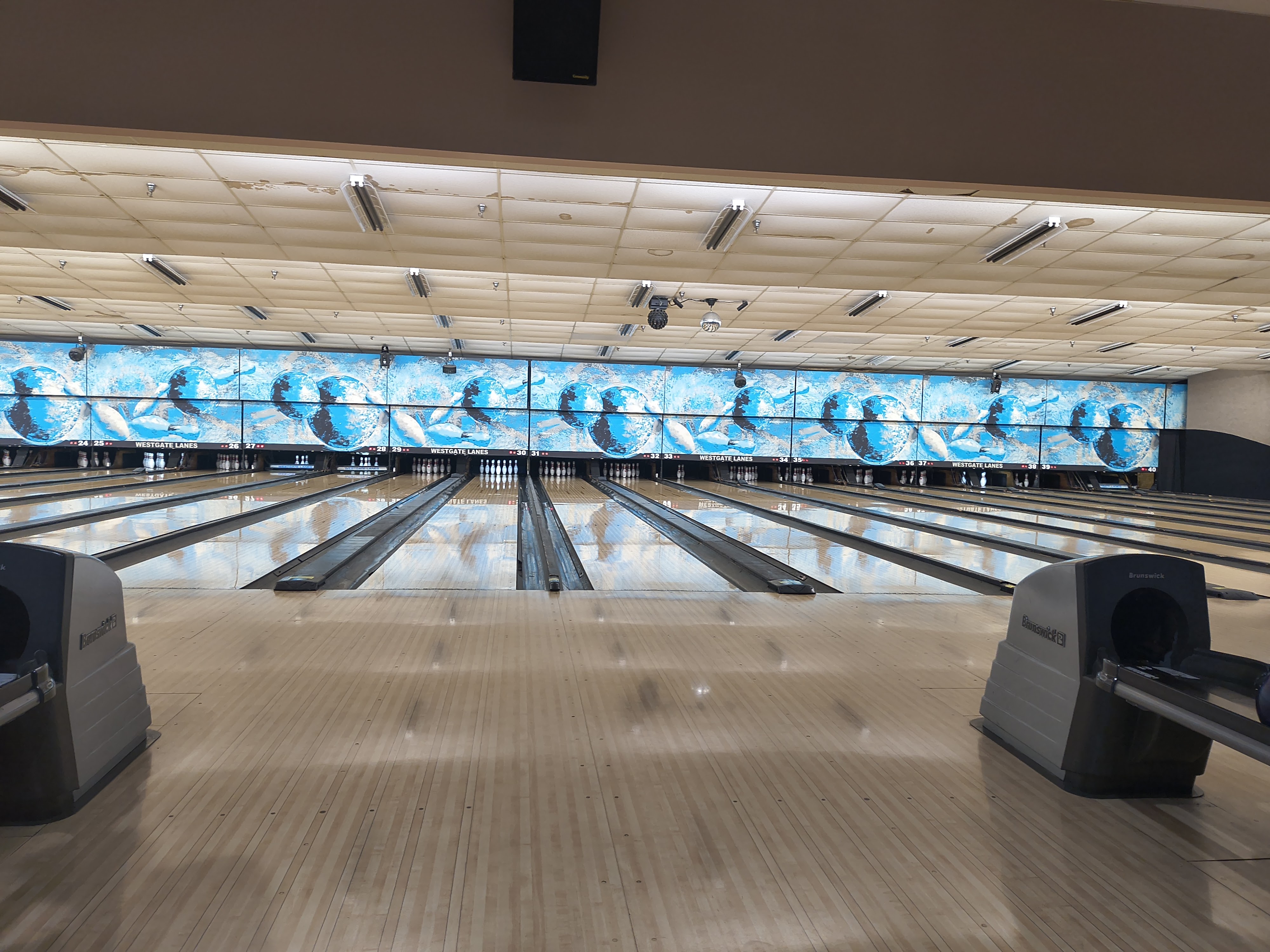 A wide view of polished bowling lanes with blue and white graphics above the pins at Westgate Lanes.