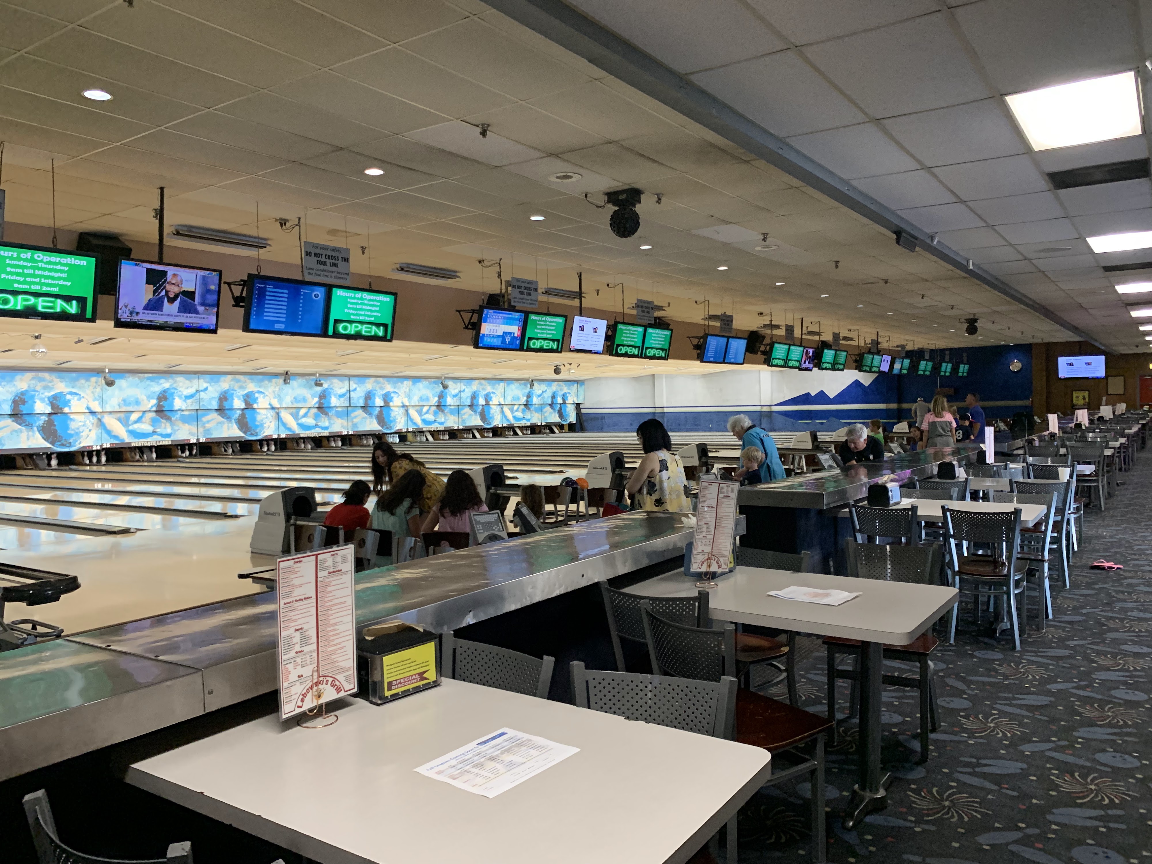 An indoor view of a bowling center with people at the lanes and menus on tables in the foreground.