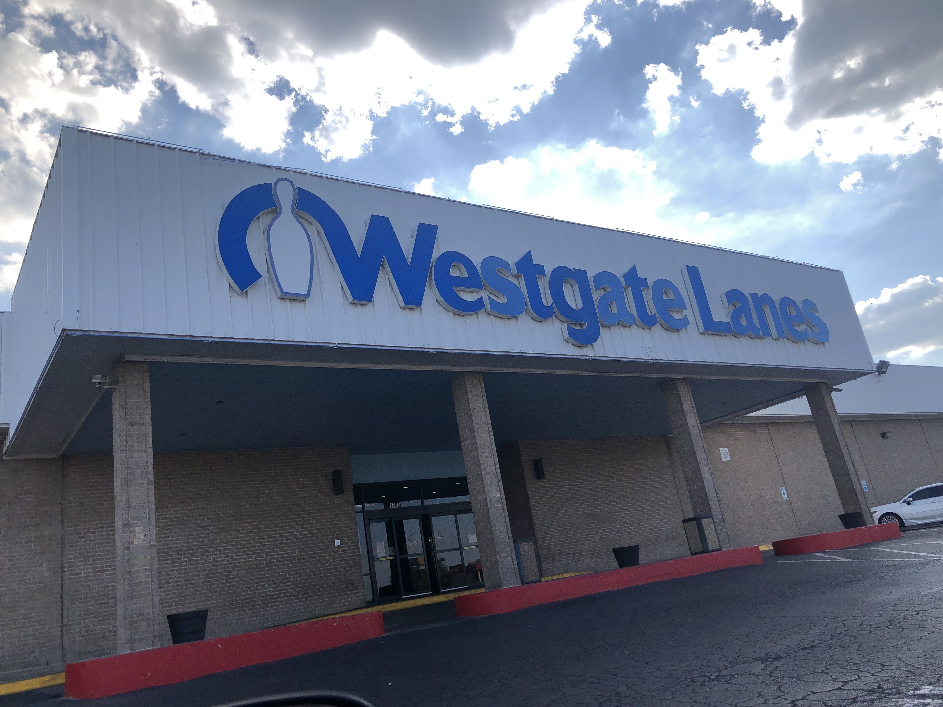 Exterior view of Westgate Lanes featuring a large blue sign and a bowling pin logo on a white building.