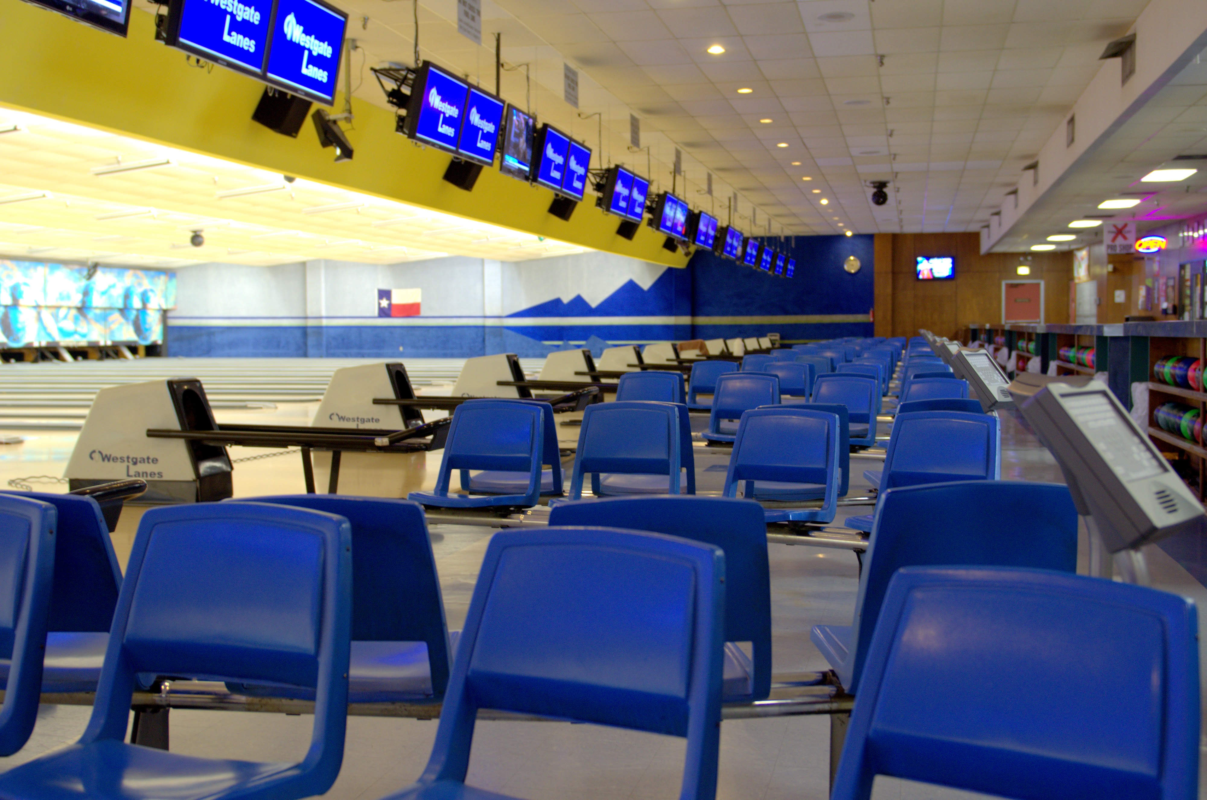 Empty bowling lanes at Westgate Lanes featuring blue seating and branded overhead monitors.