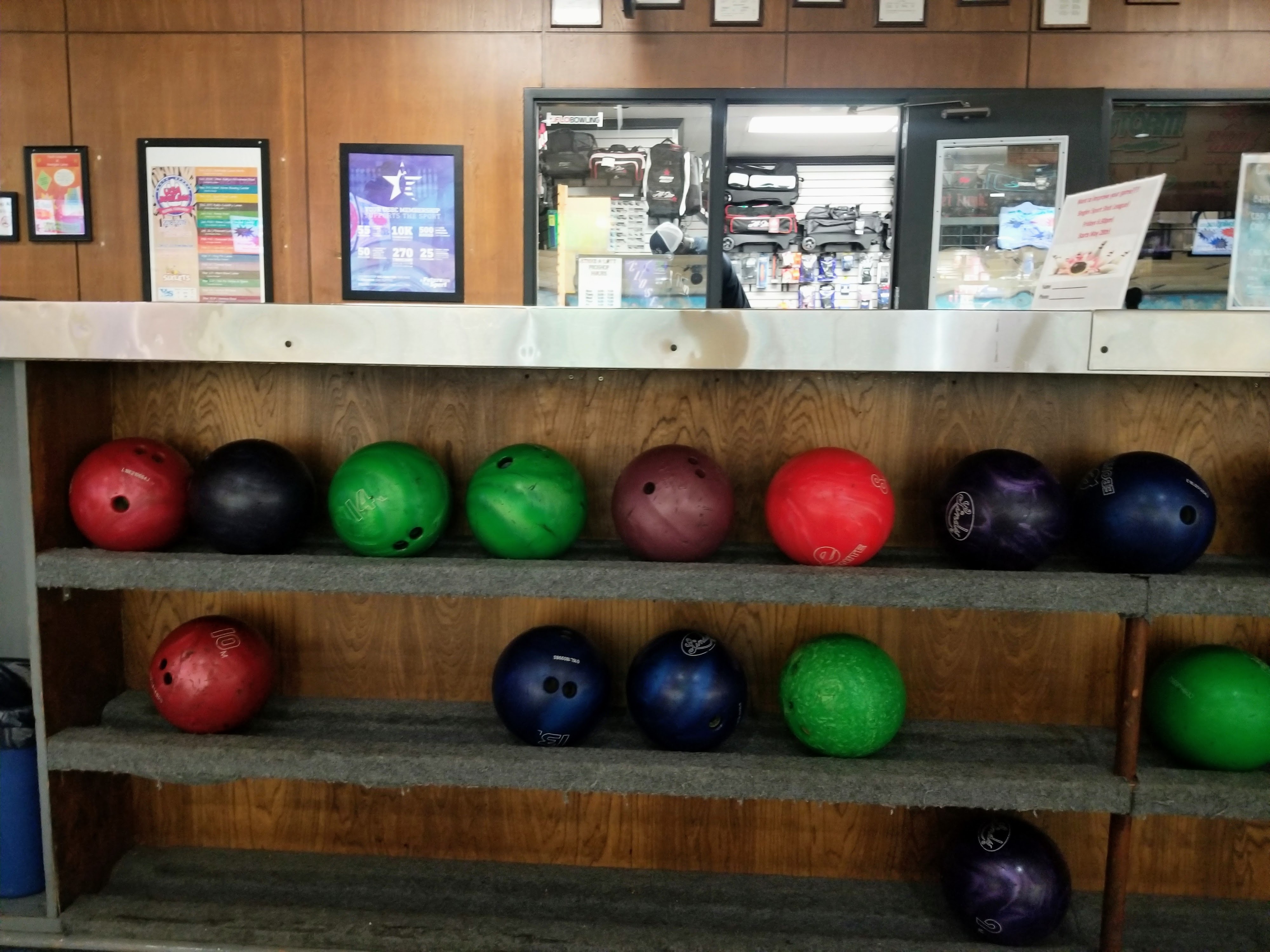 A wooden rack holding several colorful bowling balls in front of a pro shop counter.