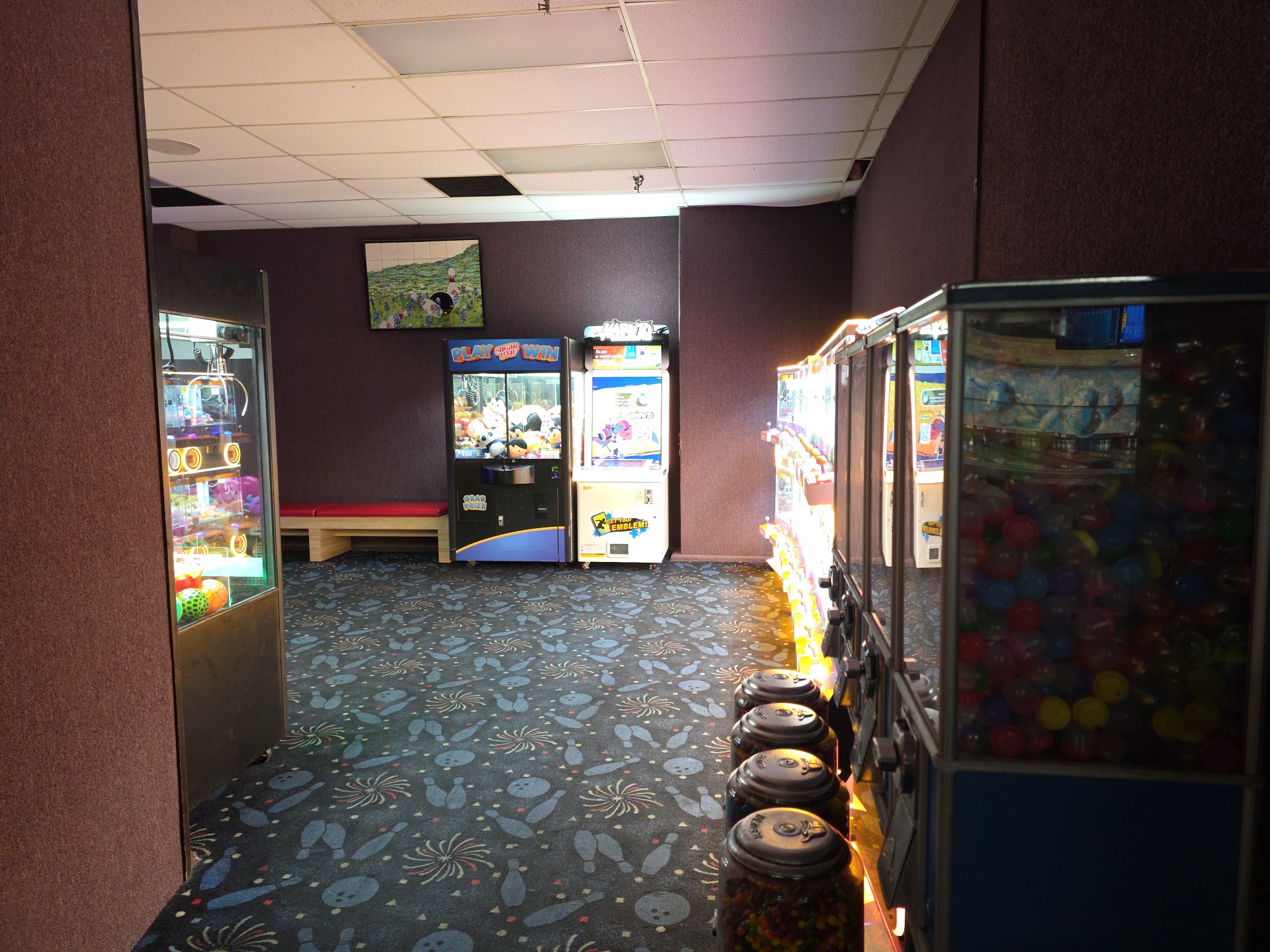 An arcade area featuring several claw machines and prize games on a bowling-themed patterned carpet.