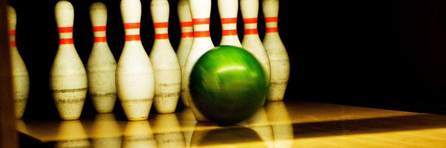 A green bowling ball rolling toward a set of ten-pin bowling pins on a polished wooden lane.