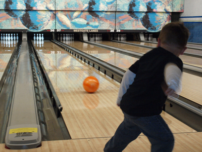 A young boy watches an orange bowling ball roll down a lane at Westgate Lanes.