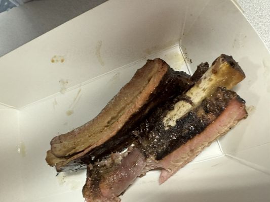 Close-up of a cooked rib and seasoned meat served in a white cardboard container.