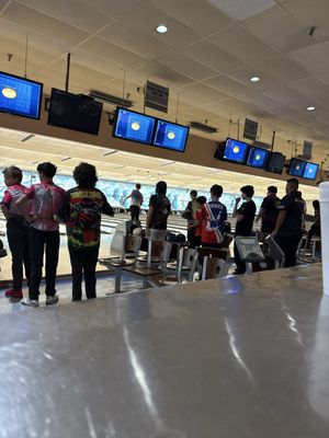 A group of young bowlers in jerseys standing at the lanes in a bowling alley.