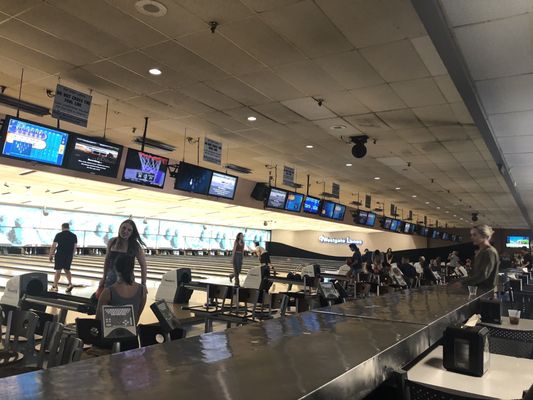 A busy bowling alley with many lanes, digital scoreboards, and people playing.
