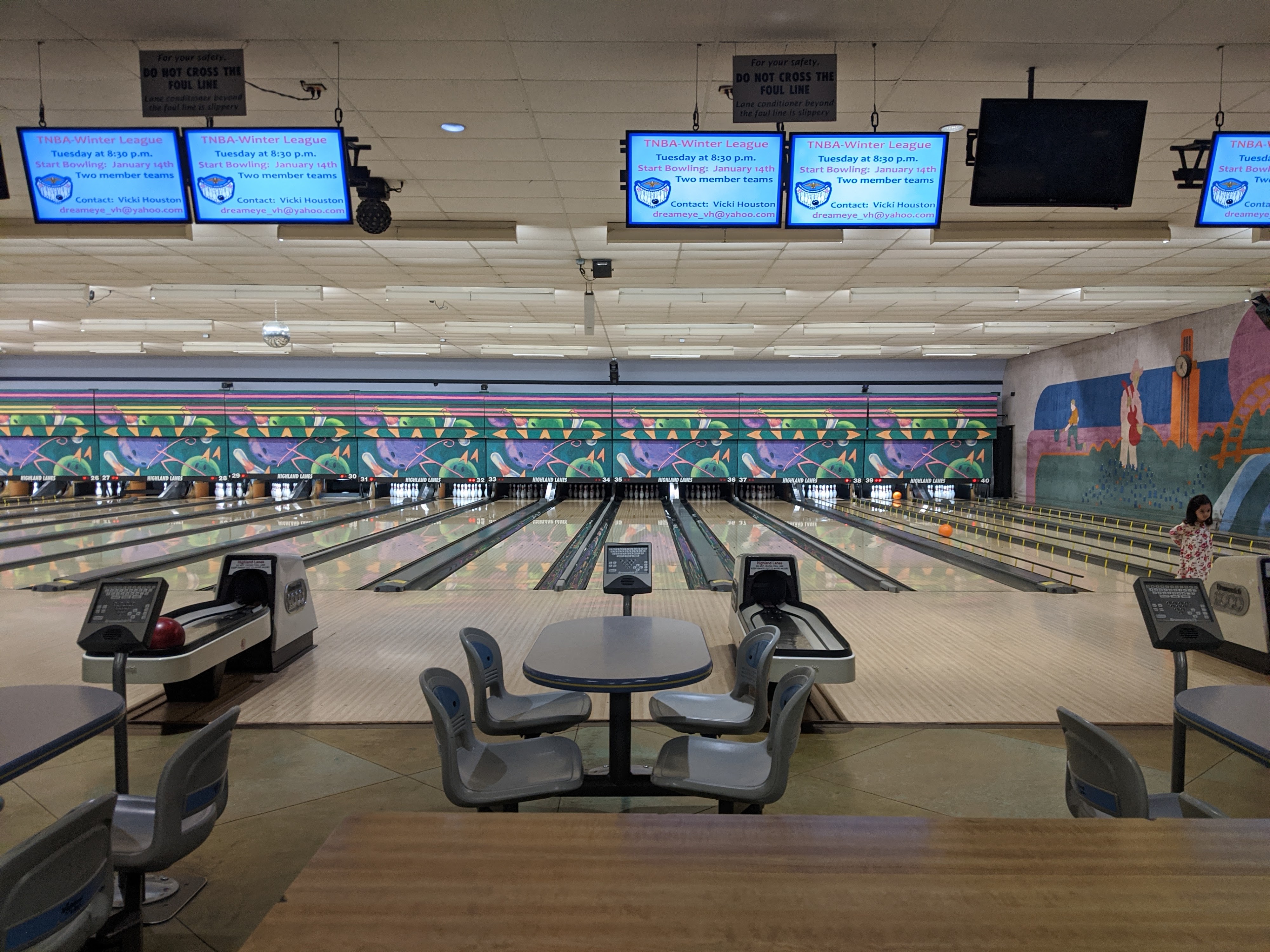 An interior view of Highland Lanes showing multiple bowling lanes, scoring monitors, and settee seating.