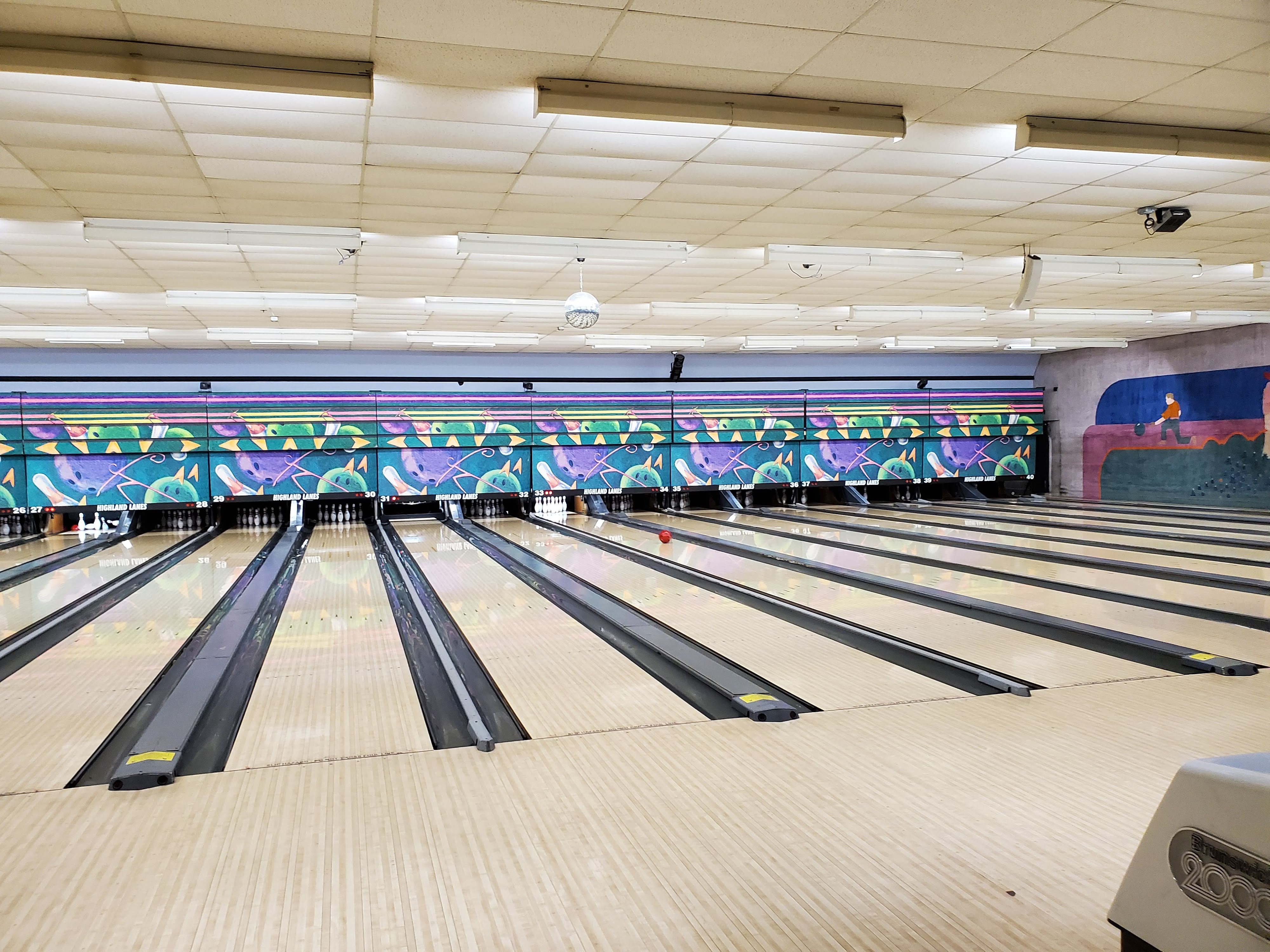 Wide view of multiple bowling lanes at Highland Lanes with a red ball rolling toward the pins.