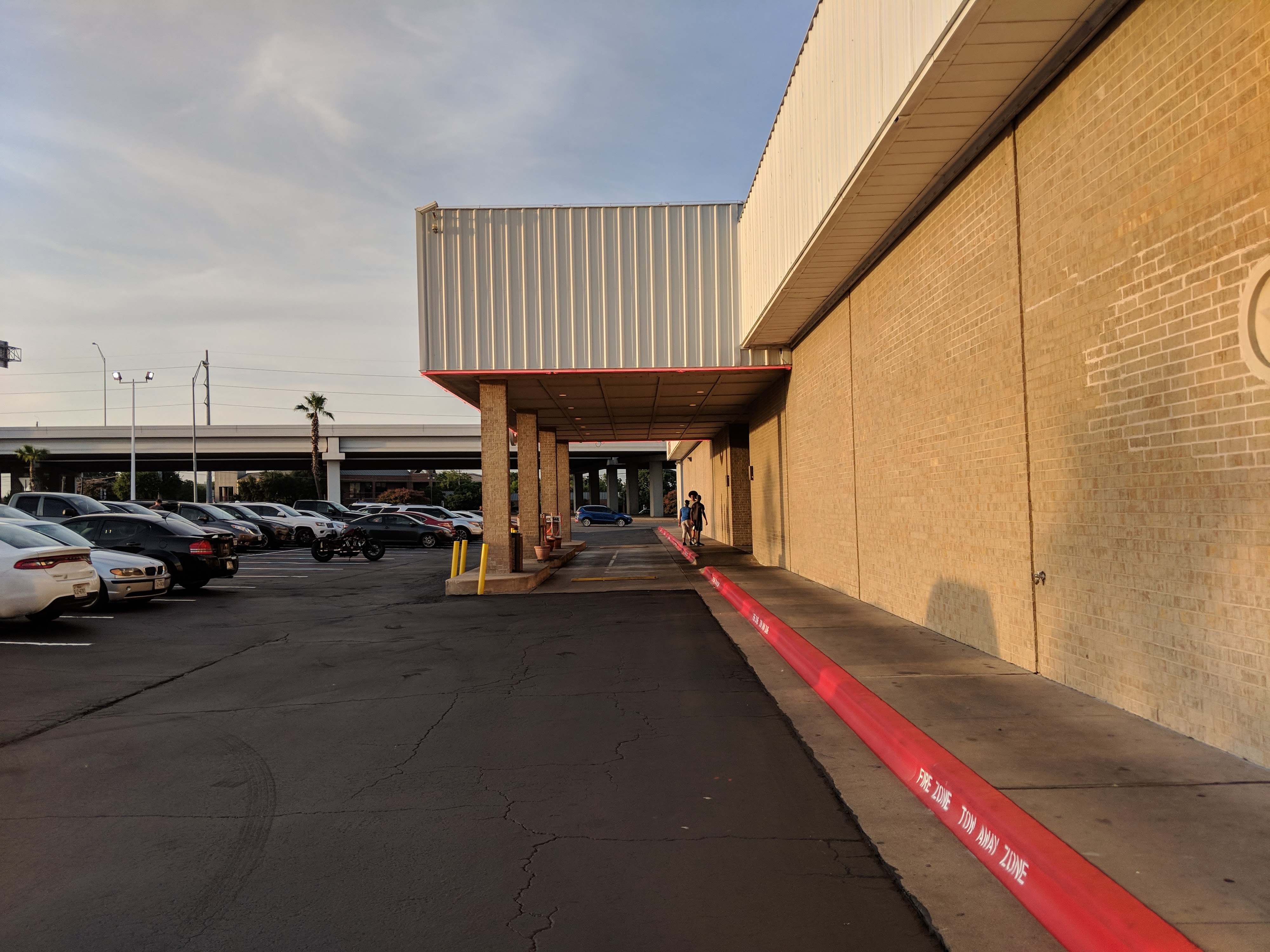 An exterior view of a tan brick building and a large paved parking lot at sunset.