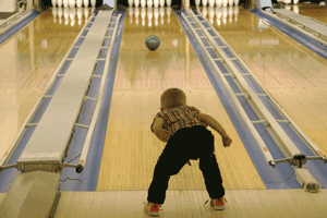 A young child watches a blue bowling ball travel down a lane with bumpers.