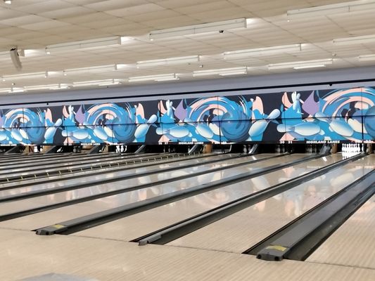 A wide view of several polished bowling lanes with a colorful blue and pink mural above the pinsetters.