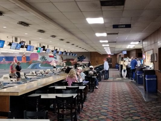 An indoor view of Highland Lanes featuring a dining area, a lounge counter, and bowling lanes with a Texas mural.