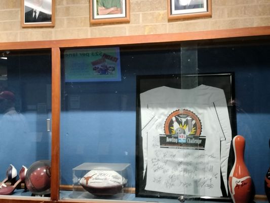 A glass display case featuring a signed NFL Alumni bowling jersey and a 2005 Texas Longhorns championship football.