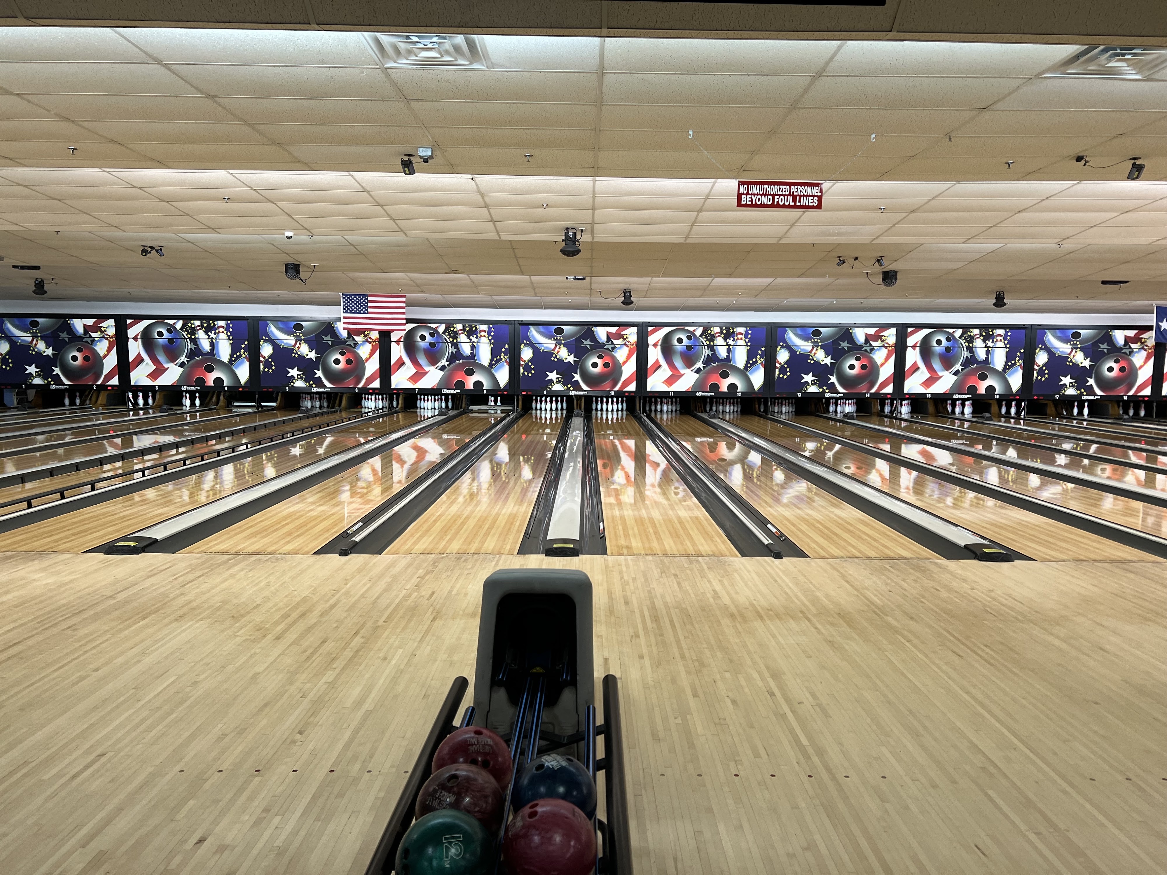 Wide view of polished bowling lanes and a ball return with colored house balls at Hallmark Lanes.