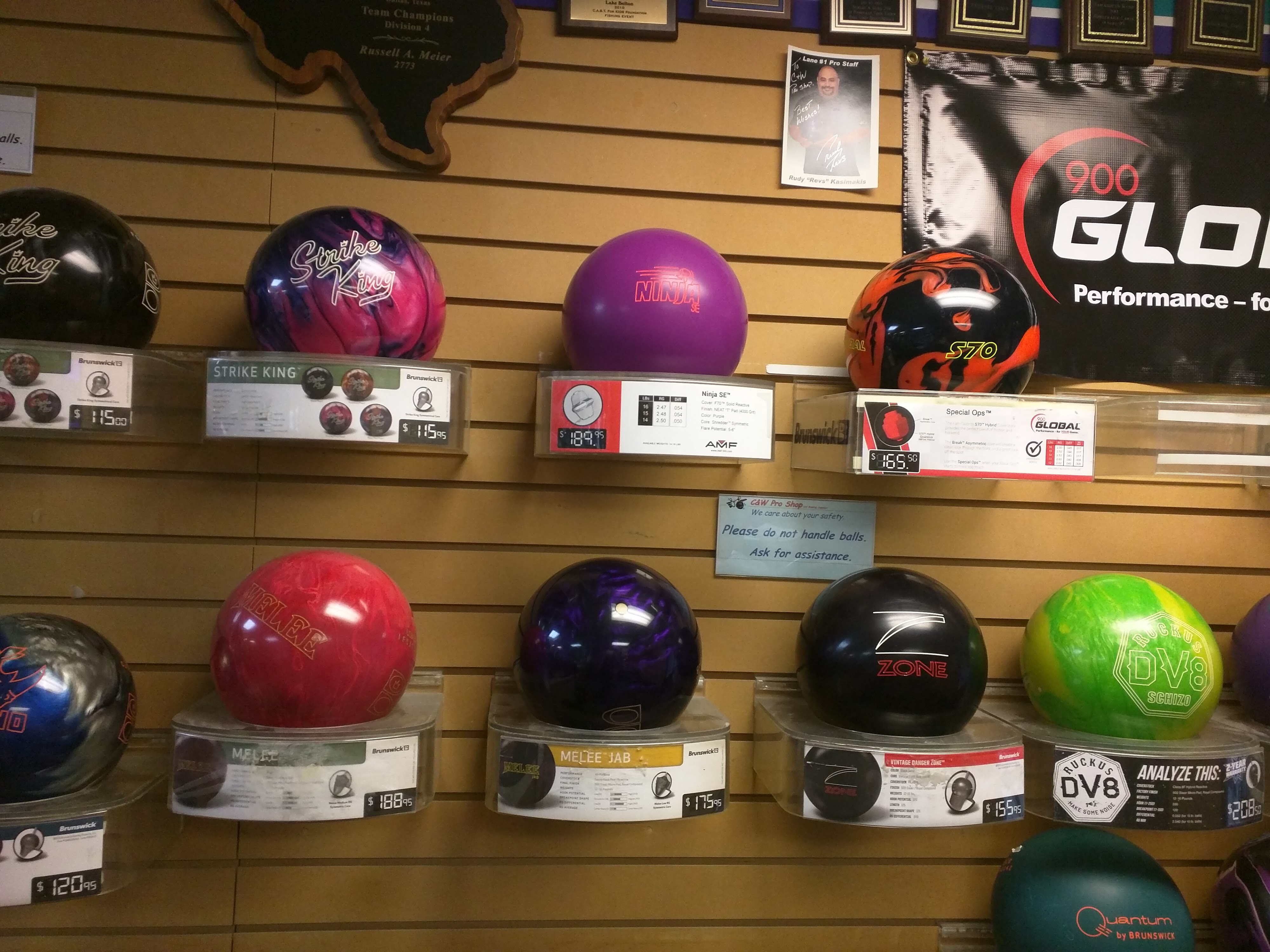 A retail display of various colorful bowling balls on shelves with price tags in a pro shop.