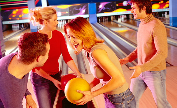 Four smiling adults picking out bowling balls at the lane ball return.