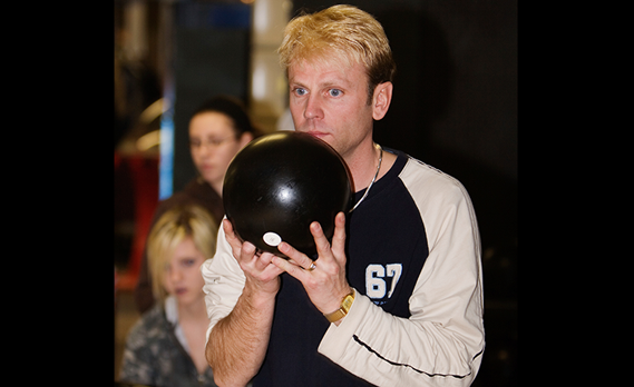 A man focuses intently while holding a black bowling ball at the approach.