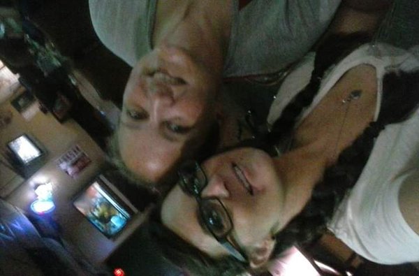 A blurry, sideways selfie of two women smiling inside a dimly lit venue with television monitors in the background.