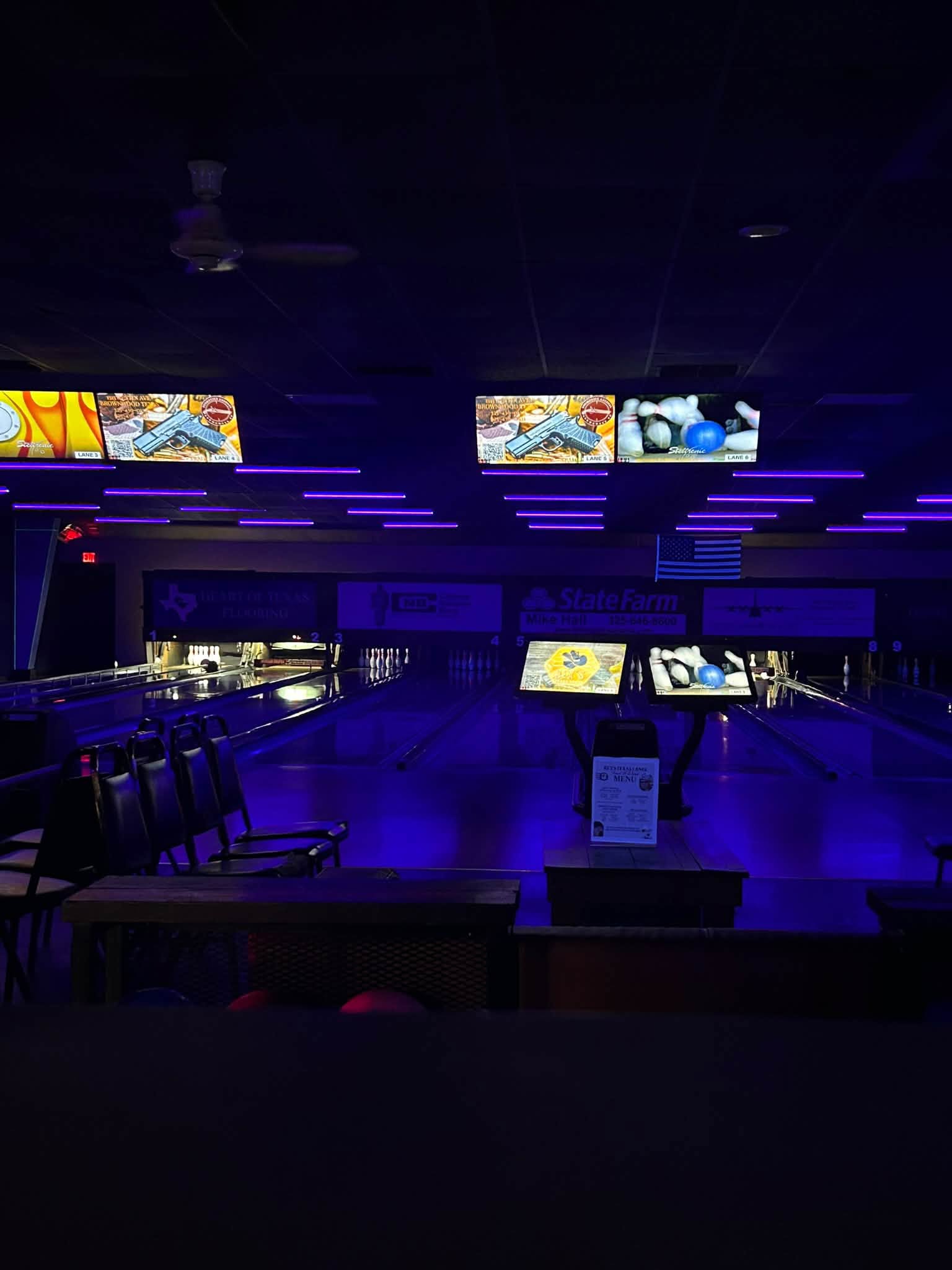 Bowling lanes at Rex's Texas Lanes are lit with blue and purple cosmic lights, showing pins and scoring monitors.