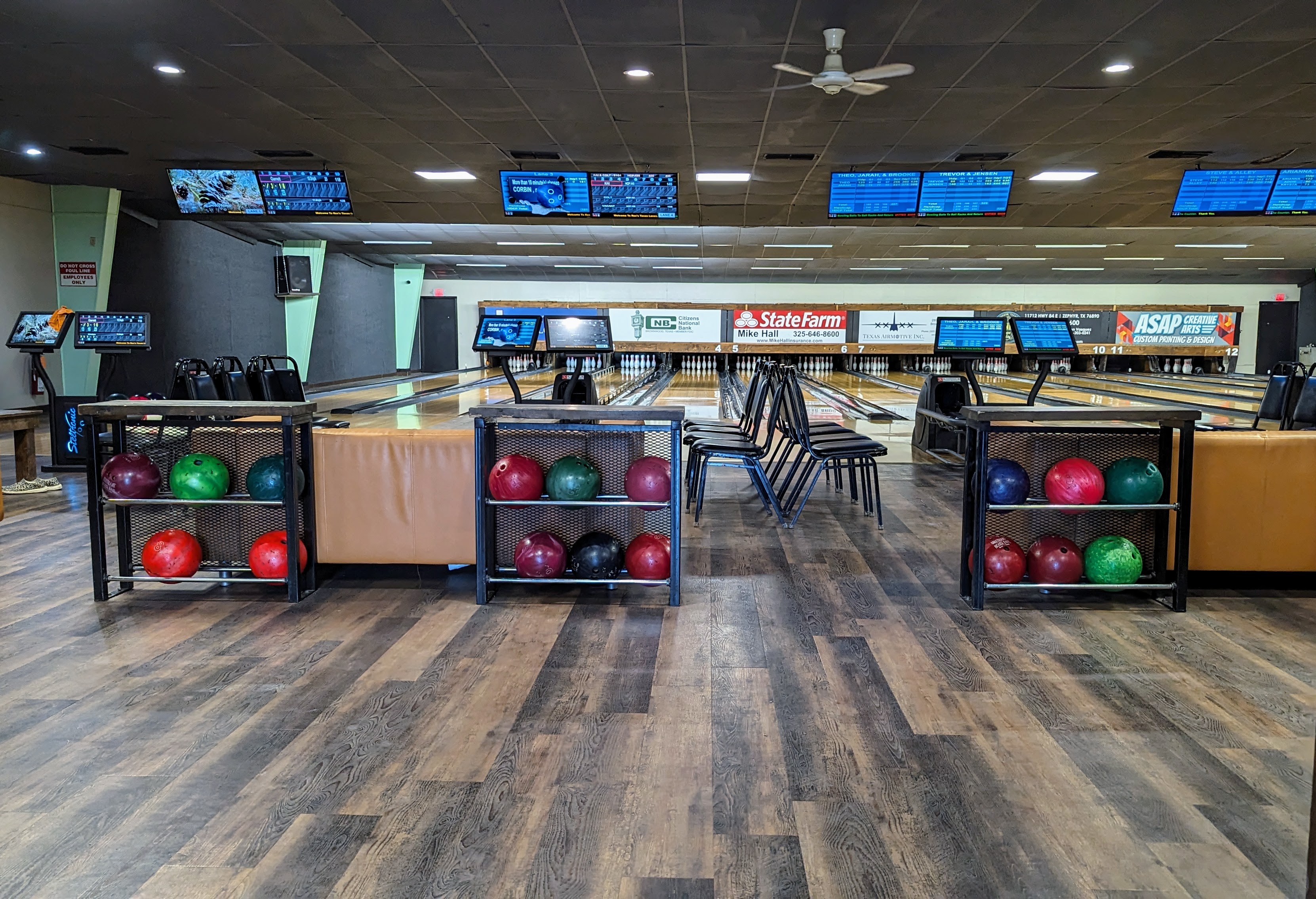 An empty bowling alley with lanes leading to pins, digital scoring screens, ball racks, and seating.