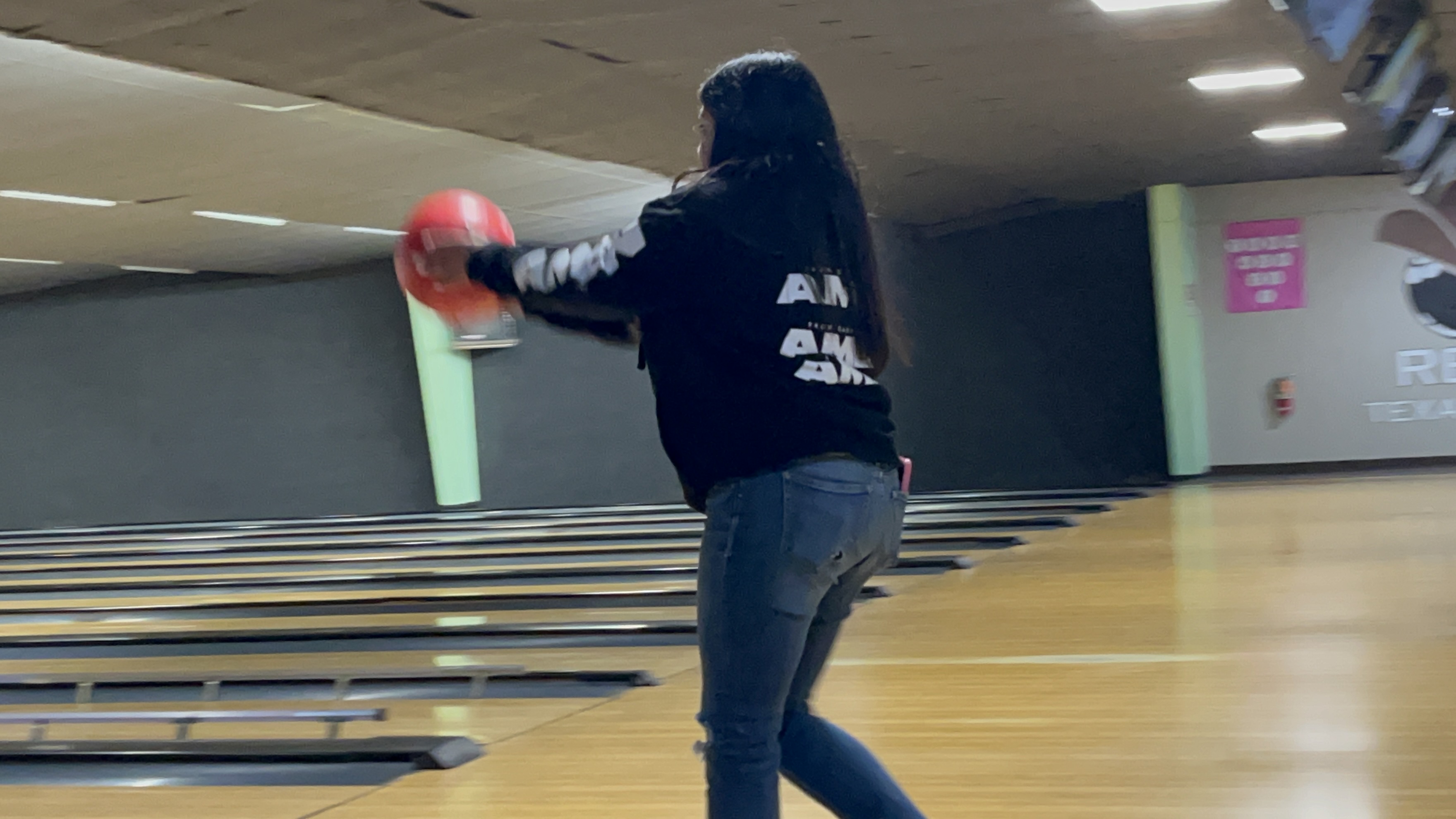 A woman bowls a red ball down a lane inside Rex's Texas Lanes.