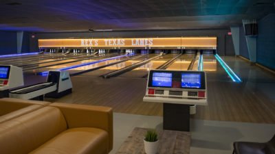 An interior view of Rex's Texas Lanes bowling alley, featuring multiple lanes, scoring monitors, and lounge seating.