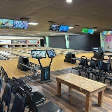 An interior view of a bowling alley with multiple lanes, seating areas, and automatic scoring screens.