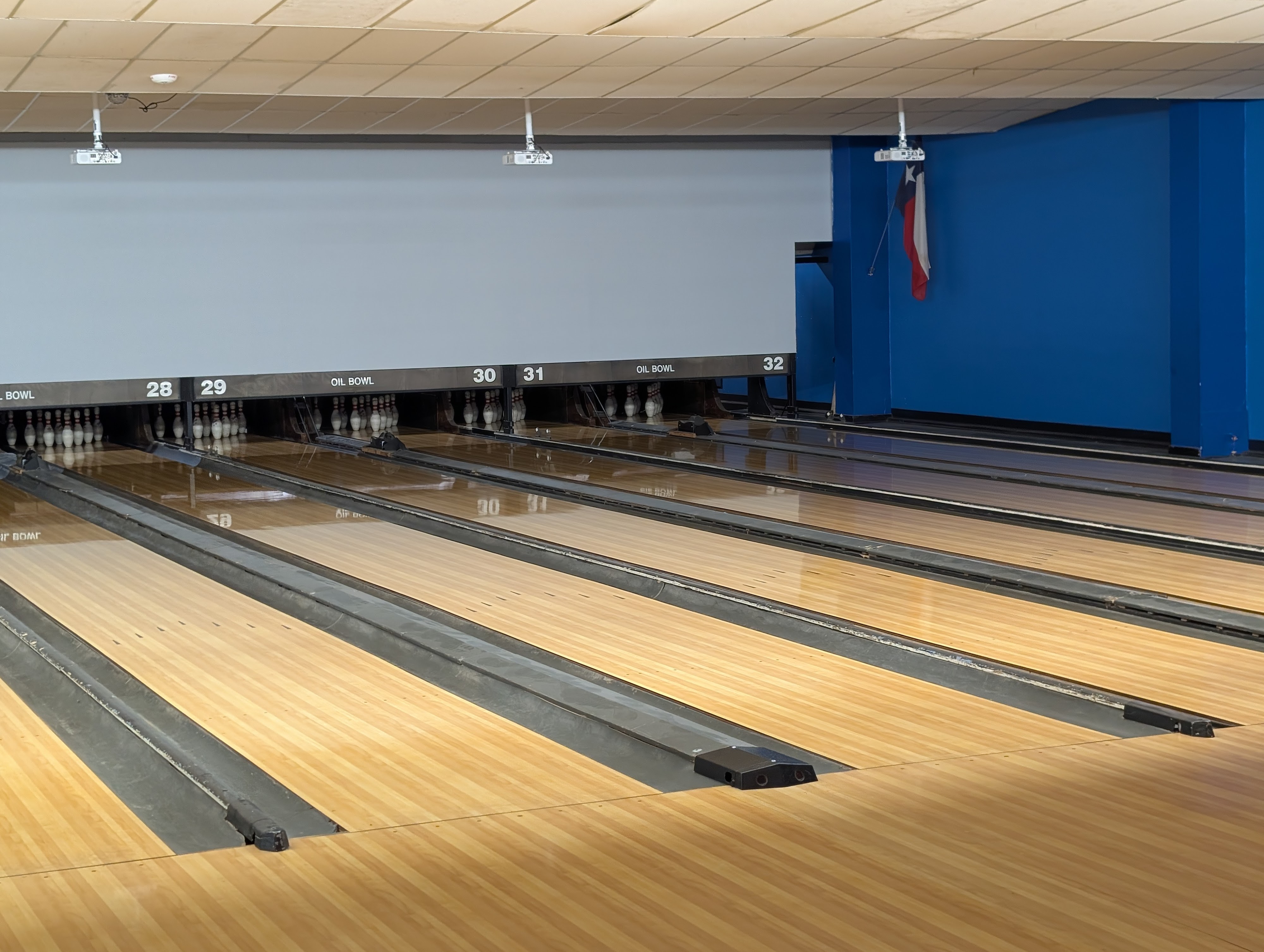 A perspective shot of several clean, wooden bowling lanes under bright lights with a Texas flag on the wall.