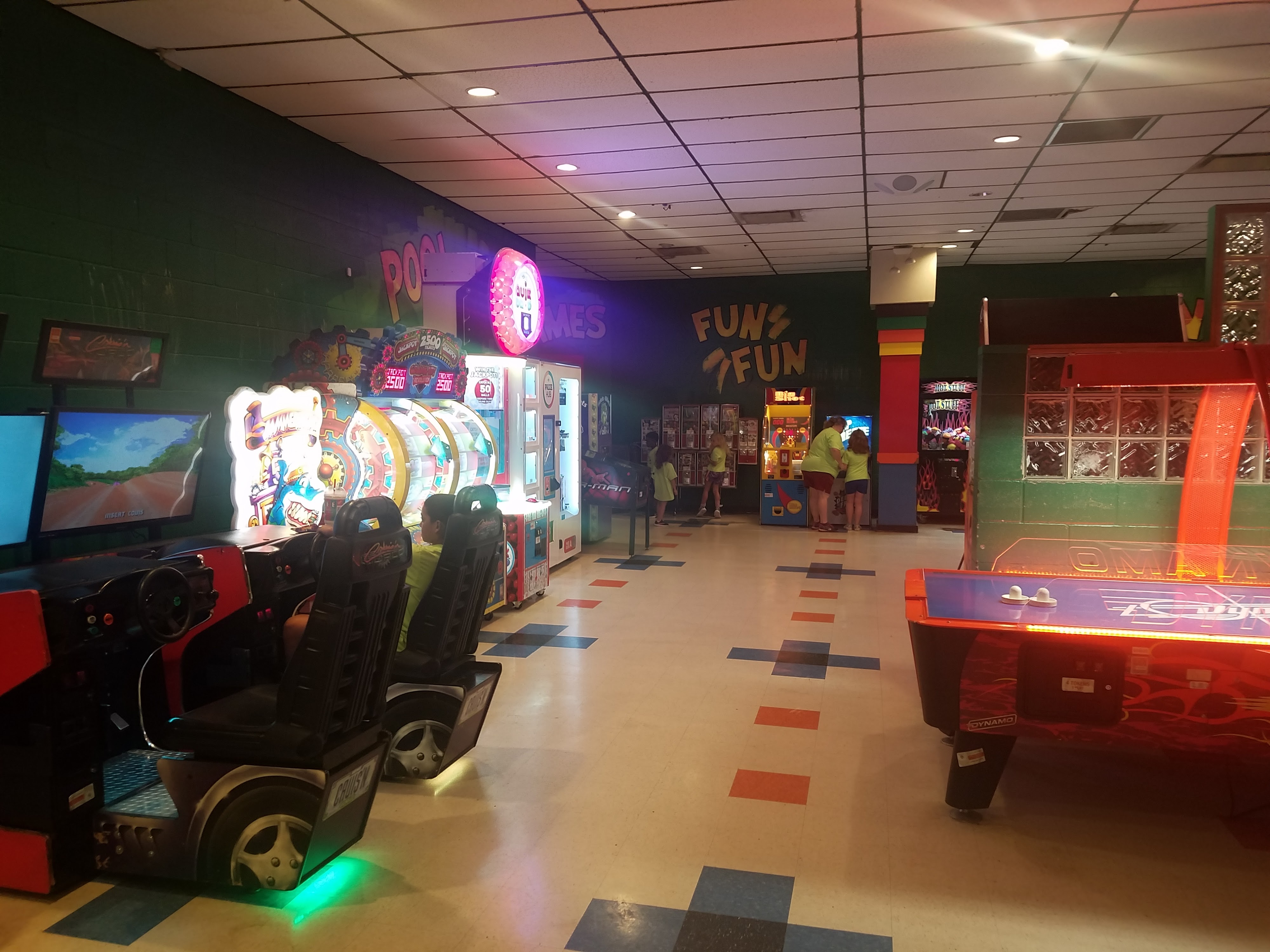 A colorful bowling center arcade featuring racing games, an air hockey table, and prize machines.