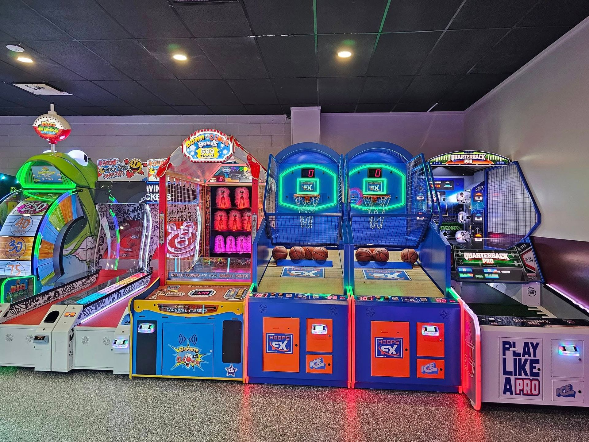 A row of colorful arcade games including basketball and football machines in a brightly lit game room.