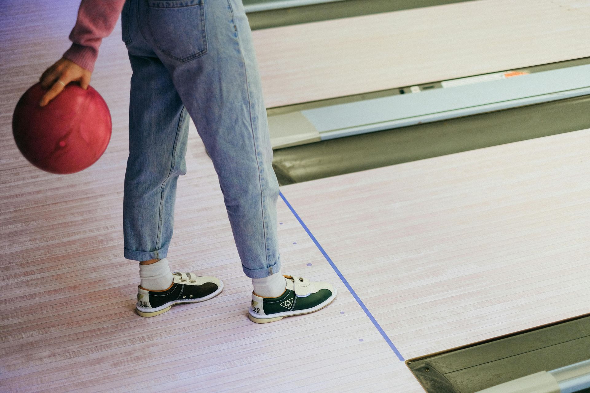 A person in bowling shoes holds a pink bowling ball while standing on a lane at Oil Bowl Lanes.