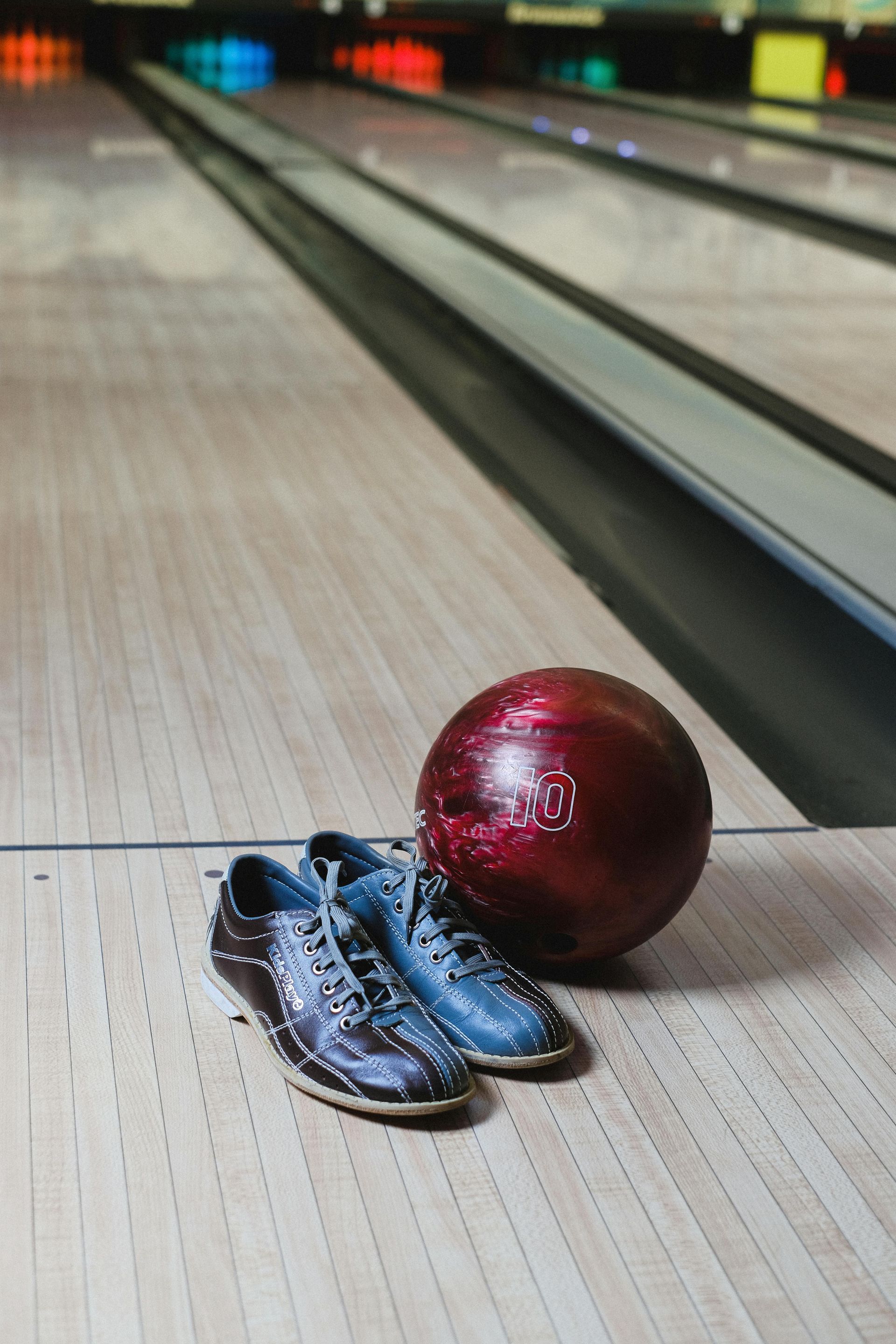 A red number ten bowling ball and a pair of rental bowling shoes sit on a wooden lane.