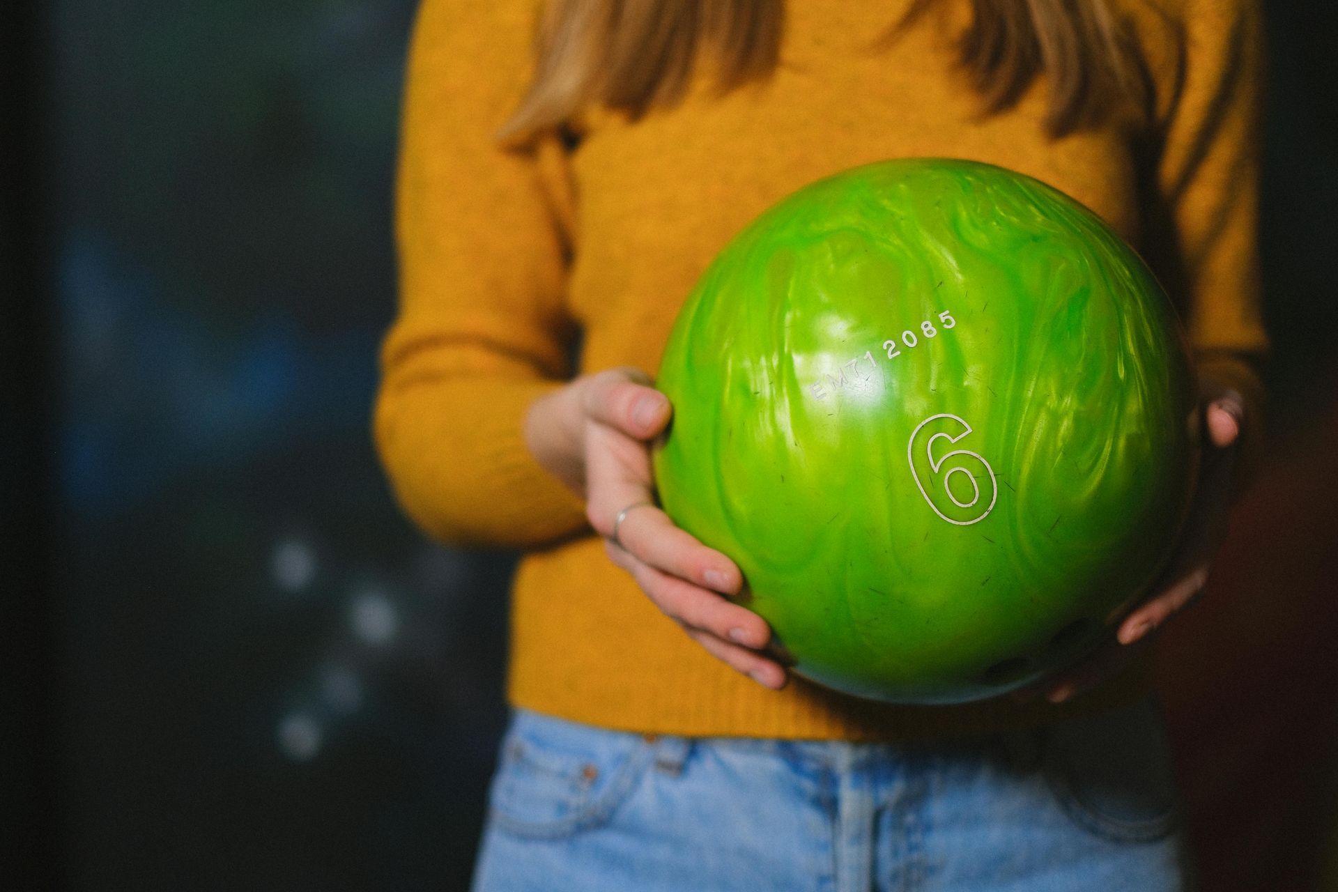 Close-up of a person in a yellow sweater holding a bright green bowling ball with the number six on it.
