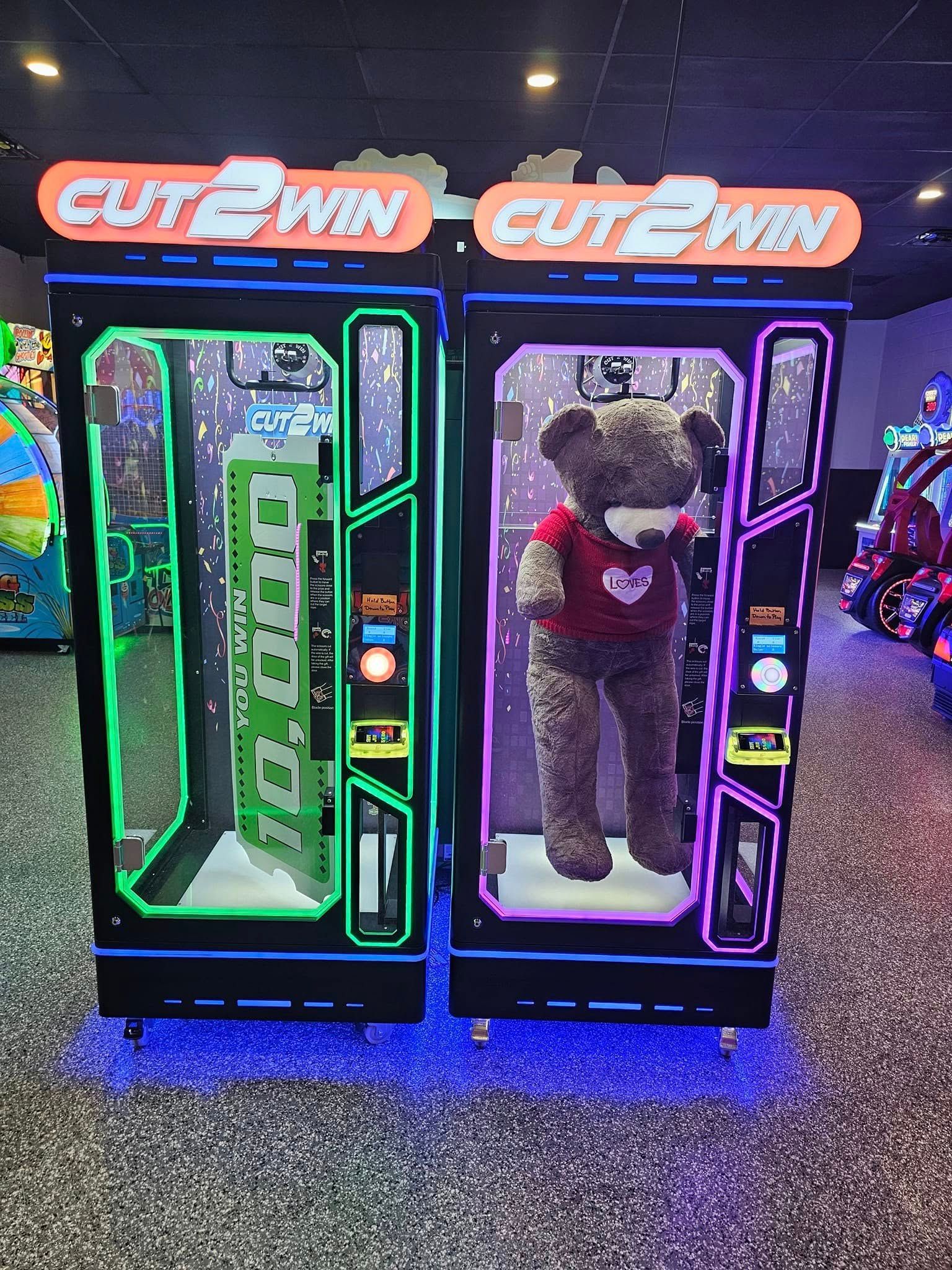 Two Cut 2 Win arcade machines with neon green and purple lights and a large teddy bear prize.