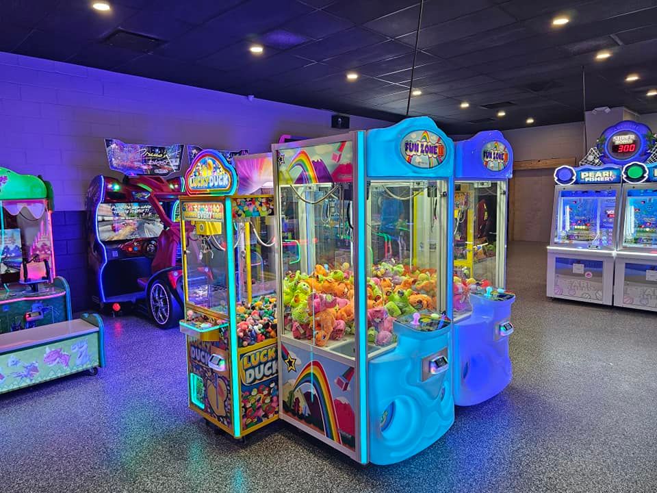 A variety of brightly lit arcade games and claw machines in a colorful recreation room.